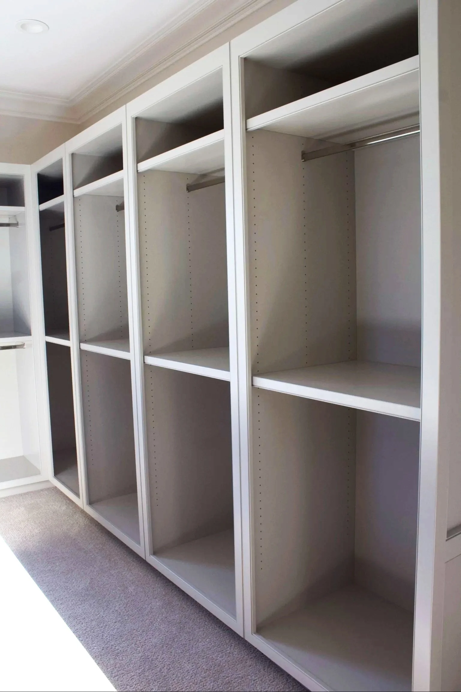 Custom closet cabinets painted Sherwin Williams Anew Gray, featuring stacked drawer island, window seats, hidden closet behind mirror, and natural stone counter tops by Crawford Cabinets
