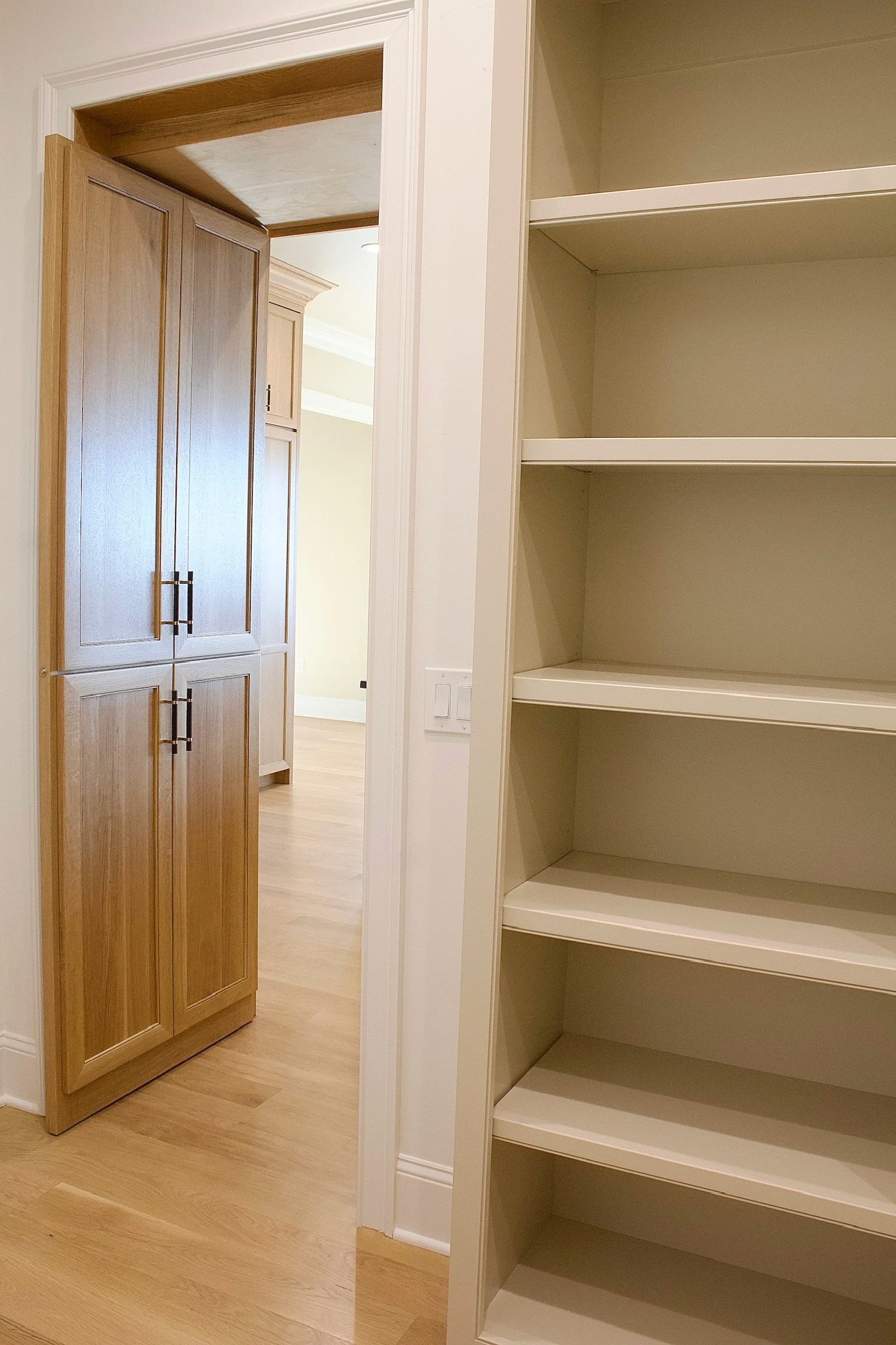 Custom hidden pantry cabinets painted Sherwin Williams Accessible Beige, featuring open shelves and natural stone counter tops by Crawford Cabinets