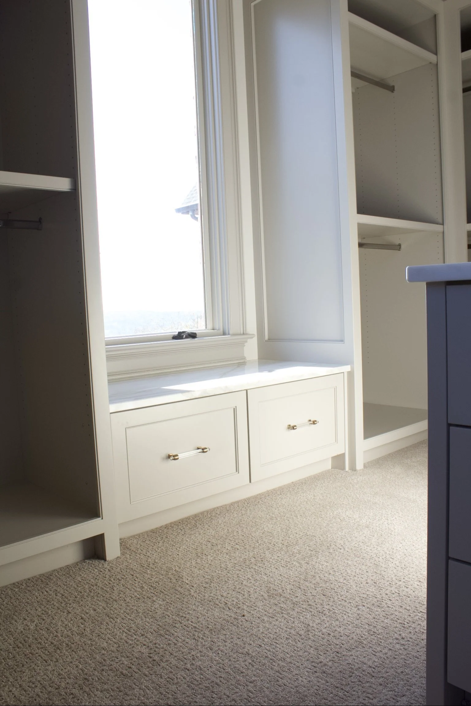 Custom closet cabinets painted Sherwin Williams Anew Gray, featuring stacked drawer island, window seats, hidden closet behind mirror, and natural stone counter tops by Crawford Cabinets