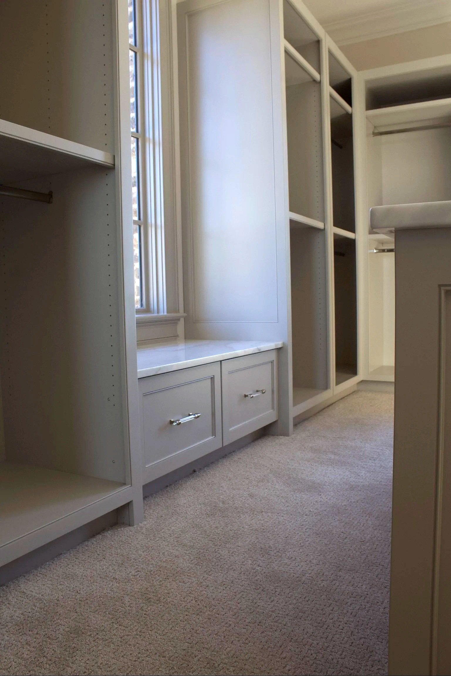 Custom closet cabinets painted Sherwin Williams Anew Gray, featuring stacked drawer island, window seats, hidden closet behind mirror, and natural stone counter tops by Crawford Cabinets