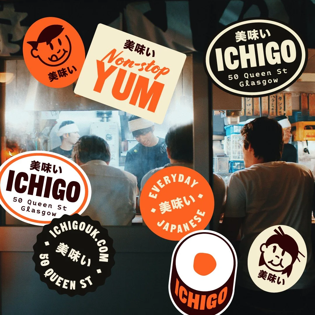 A photo of a Japanese restaurant kitchen with several people, with colorful stickers advertising Ichigo, a Japanese place on Queen Street in Glasgow, featuring phrases like "Non-stop Yum," "Everyday Japanese," and "Delicious."