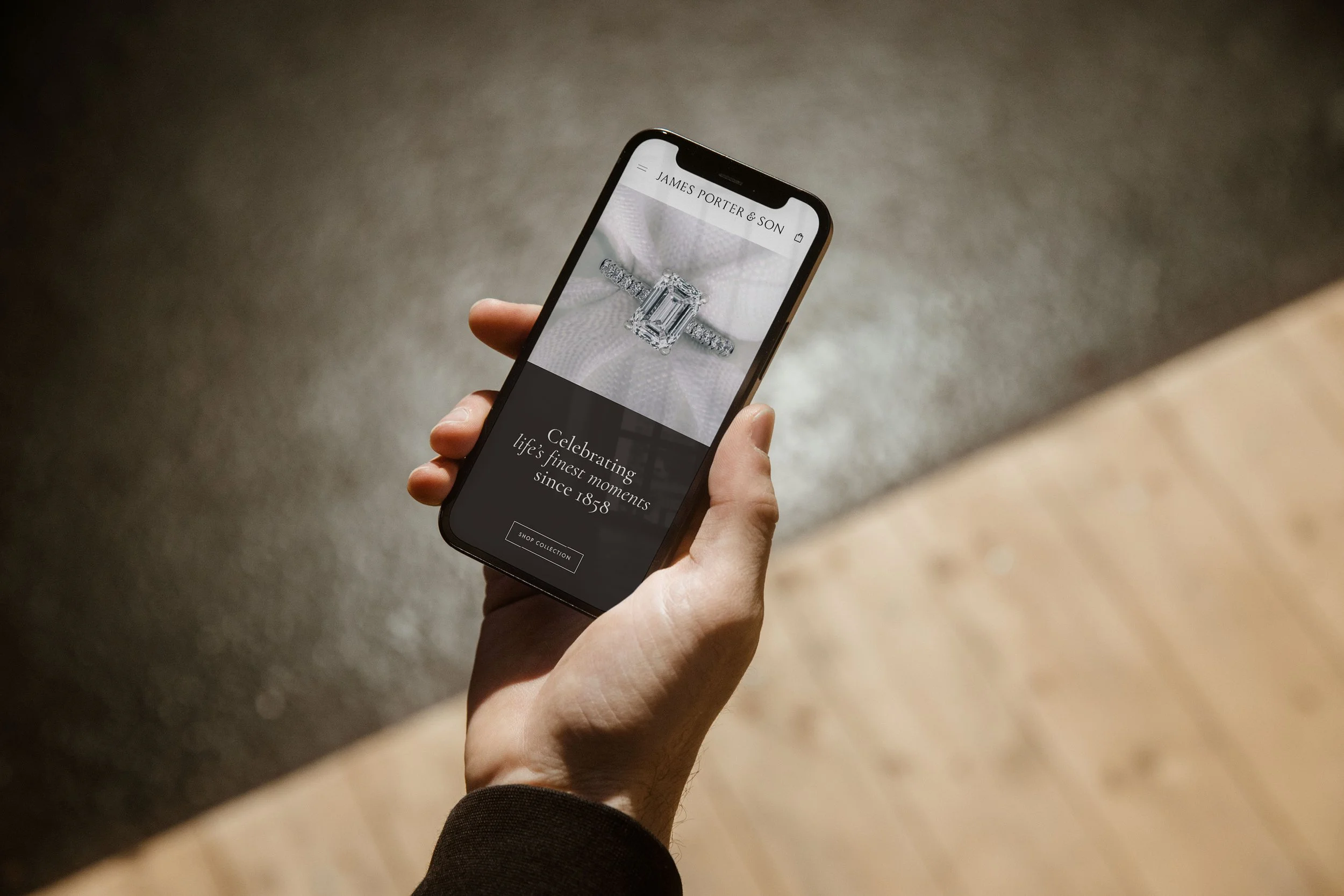 Person holding a smartphone displaying a jewelry website with an image of a diamond ring.