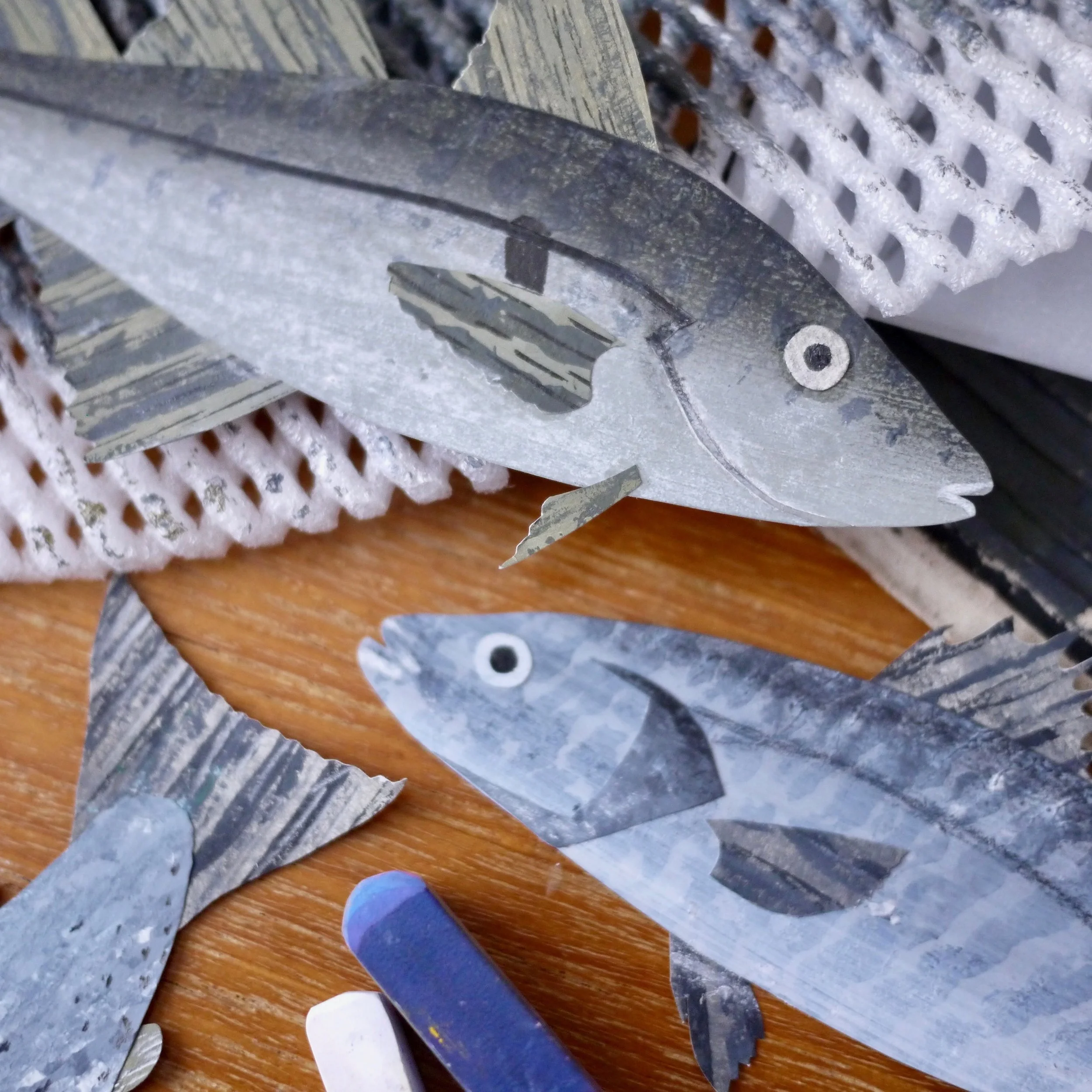 Paper fish and other paper cutouts resembling sea creatures on a wooden surface.