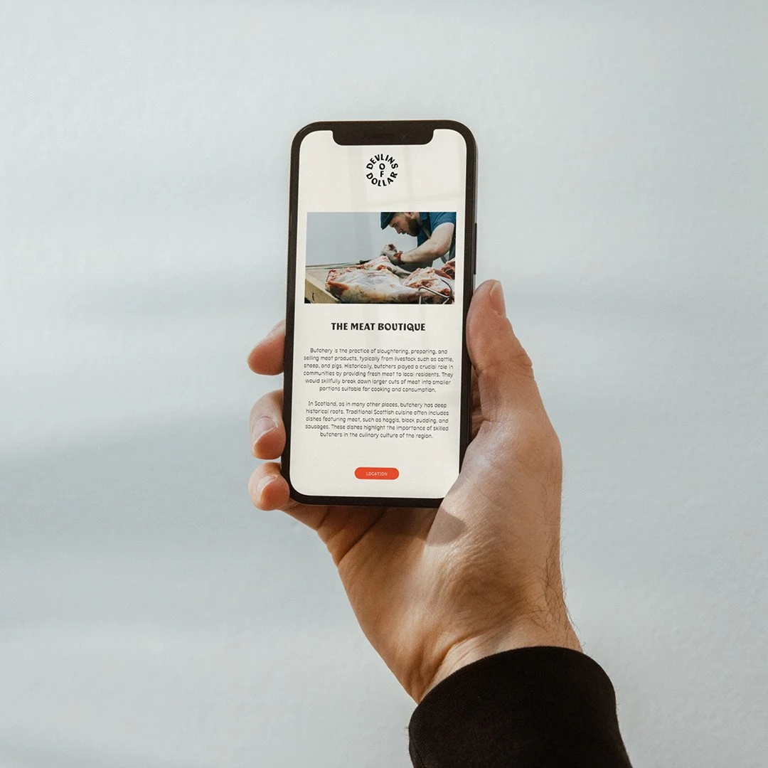 A person holding a smartphone displaying a webpage about The Meat Boutique, with an image of a butcher working with meat.