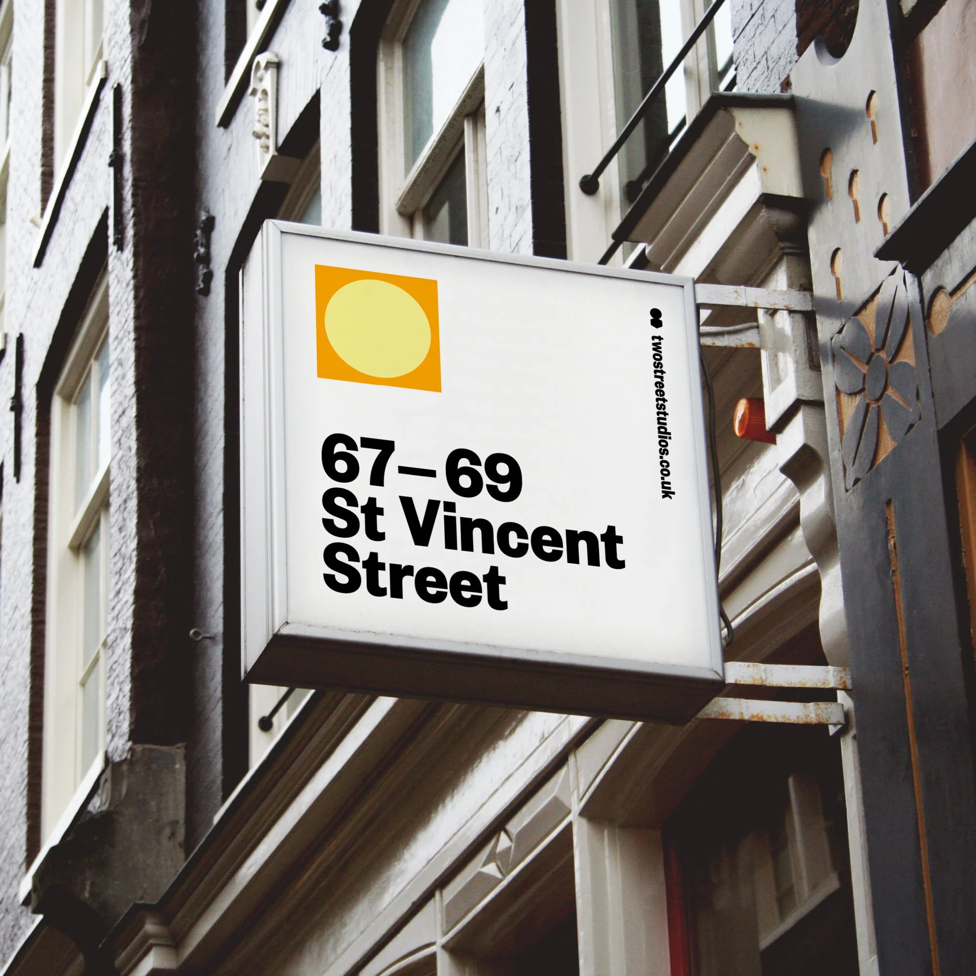 Street sign indicating addresses 67-69 St Vincent Street, attached to the side of a building with multiple windows and decorative elements, with a visible illustration of a yellow sun symbol on an orange background at the top of the sign.
