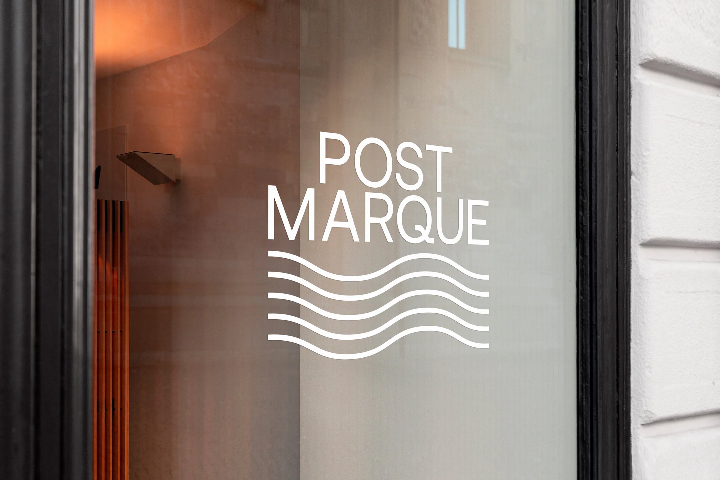 Glass door with white text and wavy lines that says 'Post Marque'