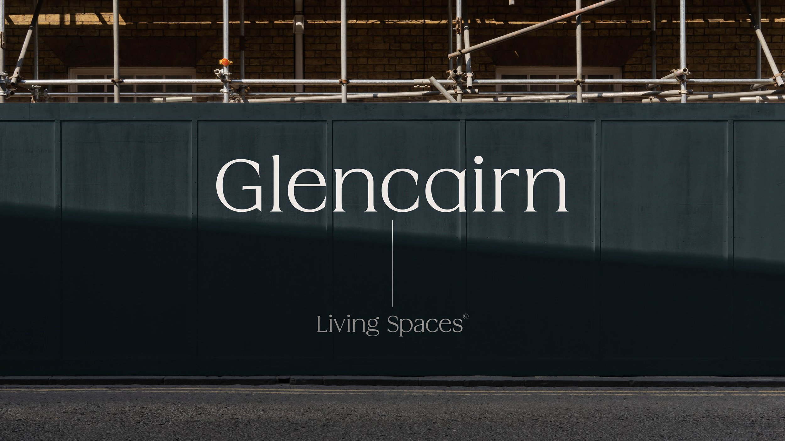 Black advertising board with white text reading 'Glencairn Living Spaces' in front of a building with brick walls and construction scaffolding.