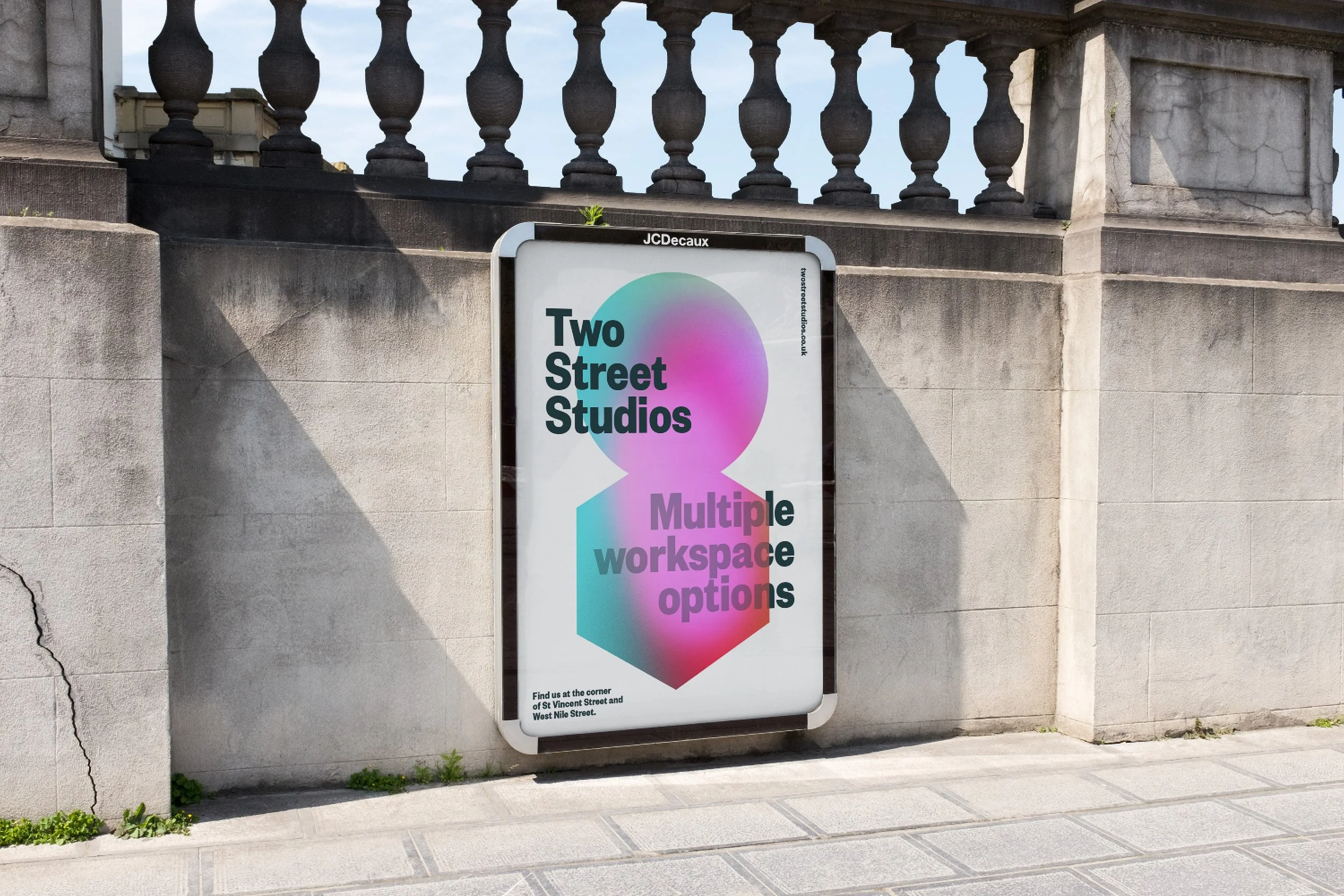 Sign advertising Two Street Studios with multiple workspace options, located on a sidewalk next to a stone wall and railing.