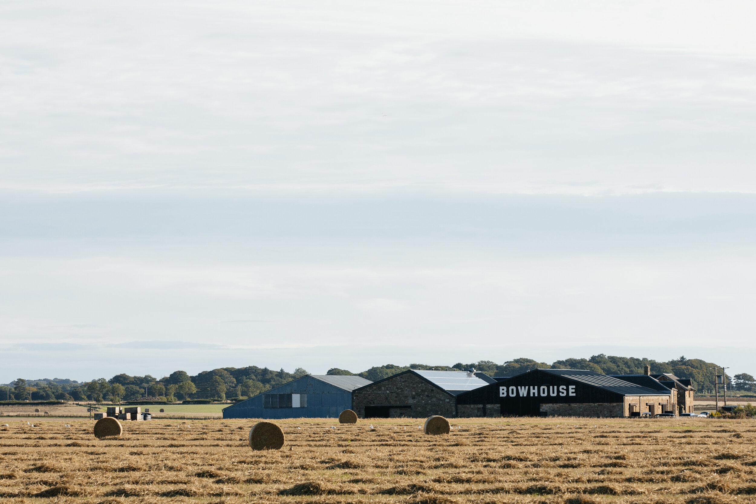 Farm field with hay bales, barn labeled 'BOWHOUSE,' and rural landscape under cloudy sky.
