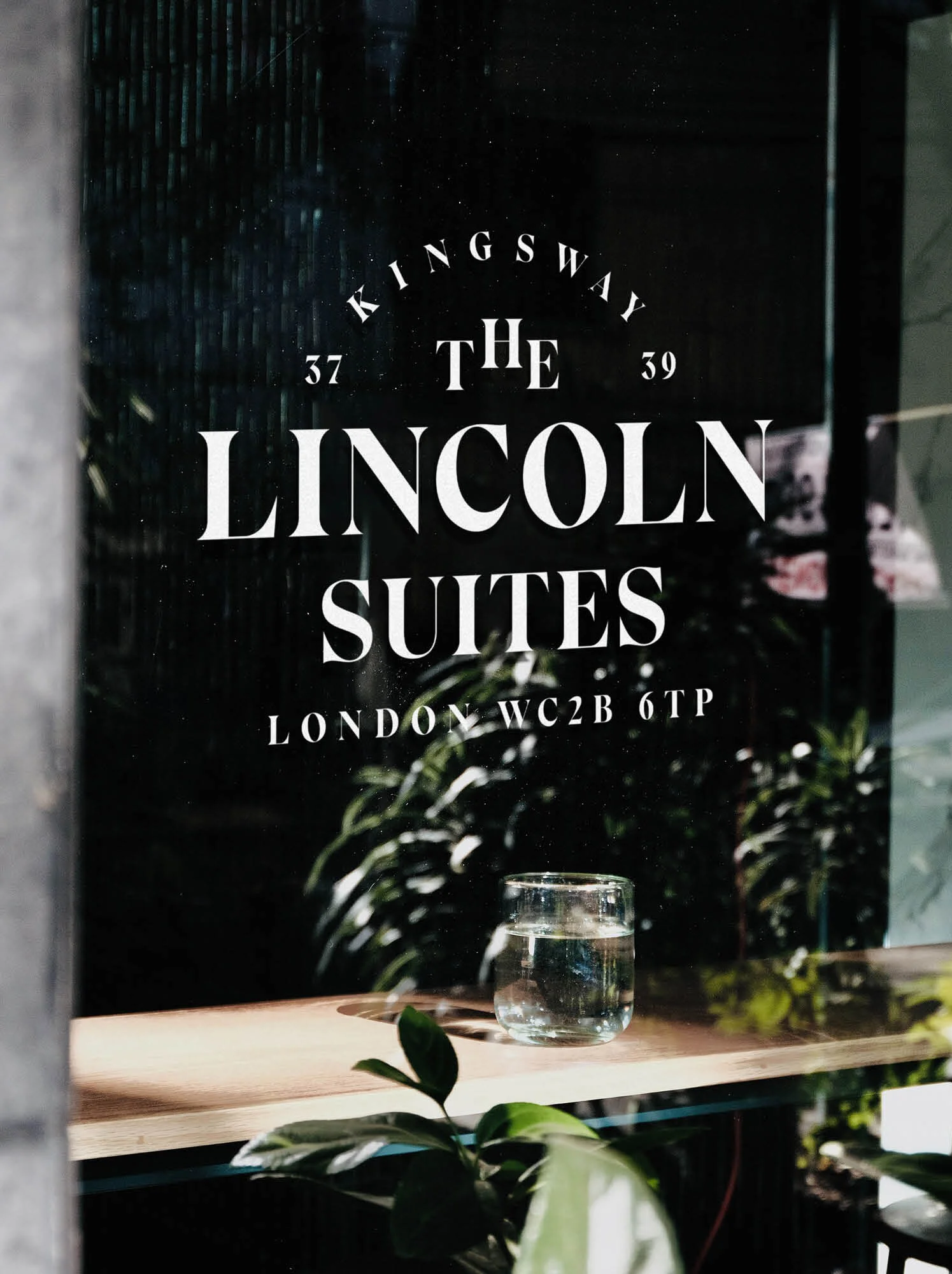 The window sign reads "The Lincoln Suites, Kingsway, London WC2B 6TP," with a glass of water and plants visible inside.