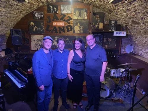 Vier Menschen stehen im Jazzclub Land mit Musikinstrumenten und einer Wand voller Jazz-Fotos im Hintergrund, festlich beleuchtet.