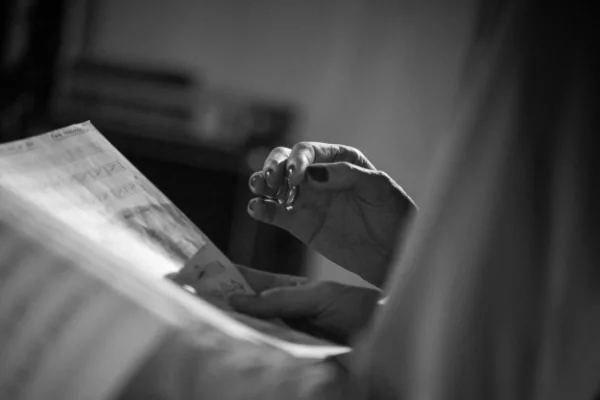Nahaufnahme einer Hand, die eine Zeitung liest, in Schwarz-Weiß-Fotografie.