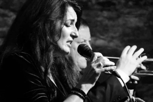 Eine Frau singt in ein Mikrofon, vermutlich bei einem Musikauftritt, schwarz-weiß