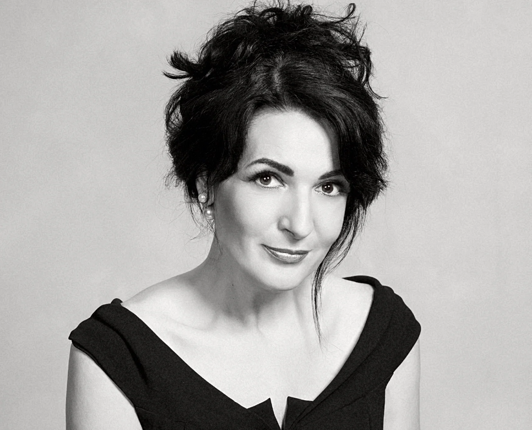 Schwarz-weiß Porträt einer Frau mit dunklen, frizzy Haaren, getragenem schwarzen Kleid und Perlenohrringen.