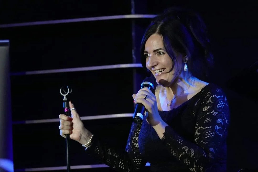 Frau beim Stand-up Comedy Auftritt auf einer Bühne, hält ein Mikrofon in der Hand.