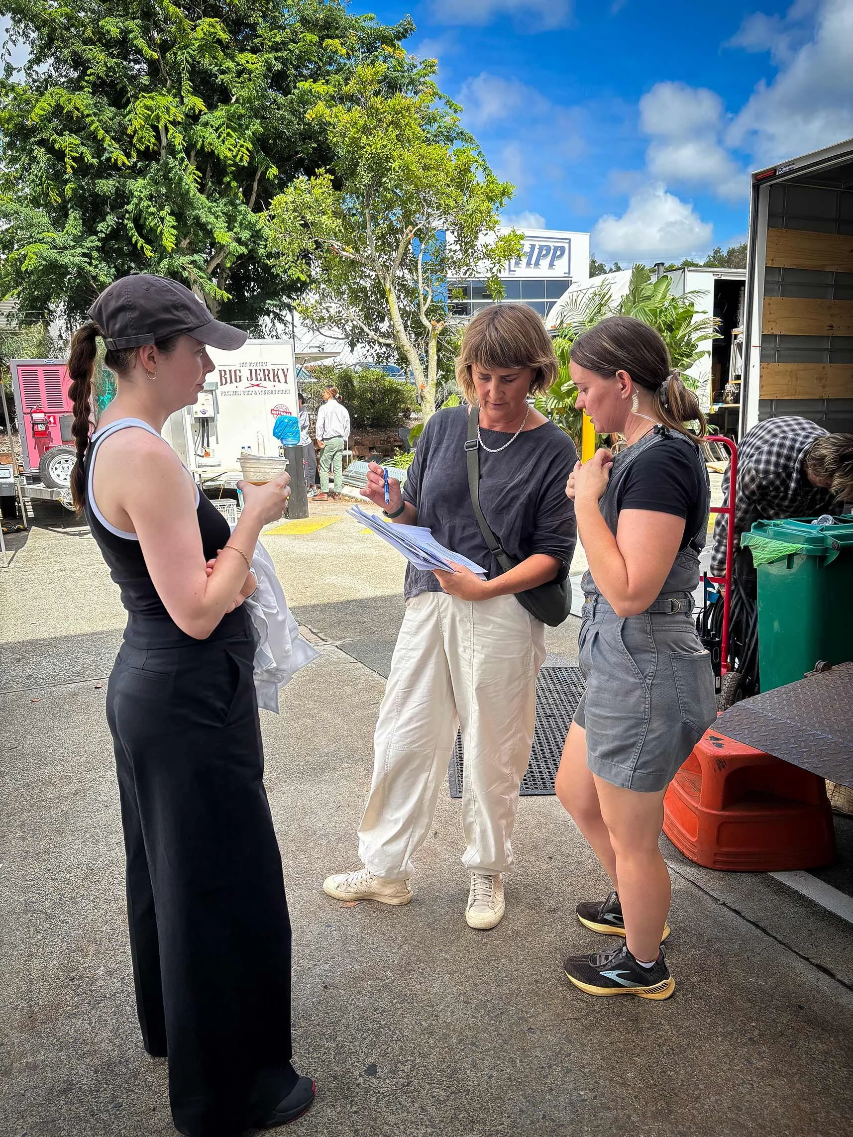 Three women standing outside on a film set, discussing the logistics for the day