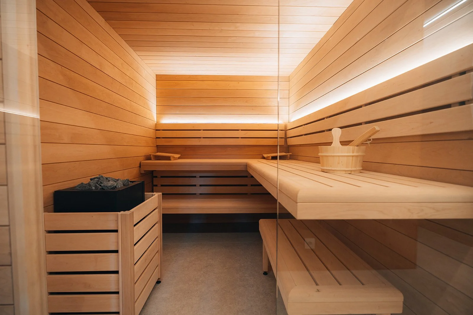 Intérieur d'un sauna en bois avec bancs en bois, seau à accessoires et pierres pour la vapeur.