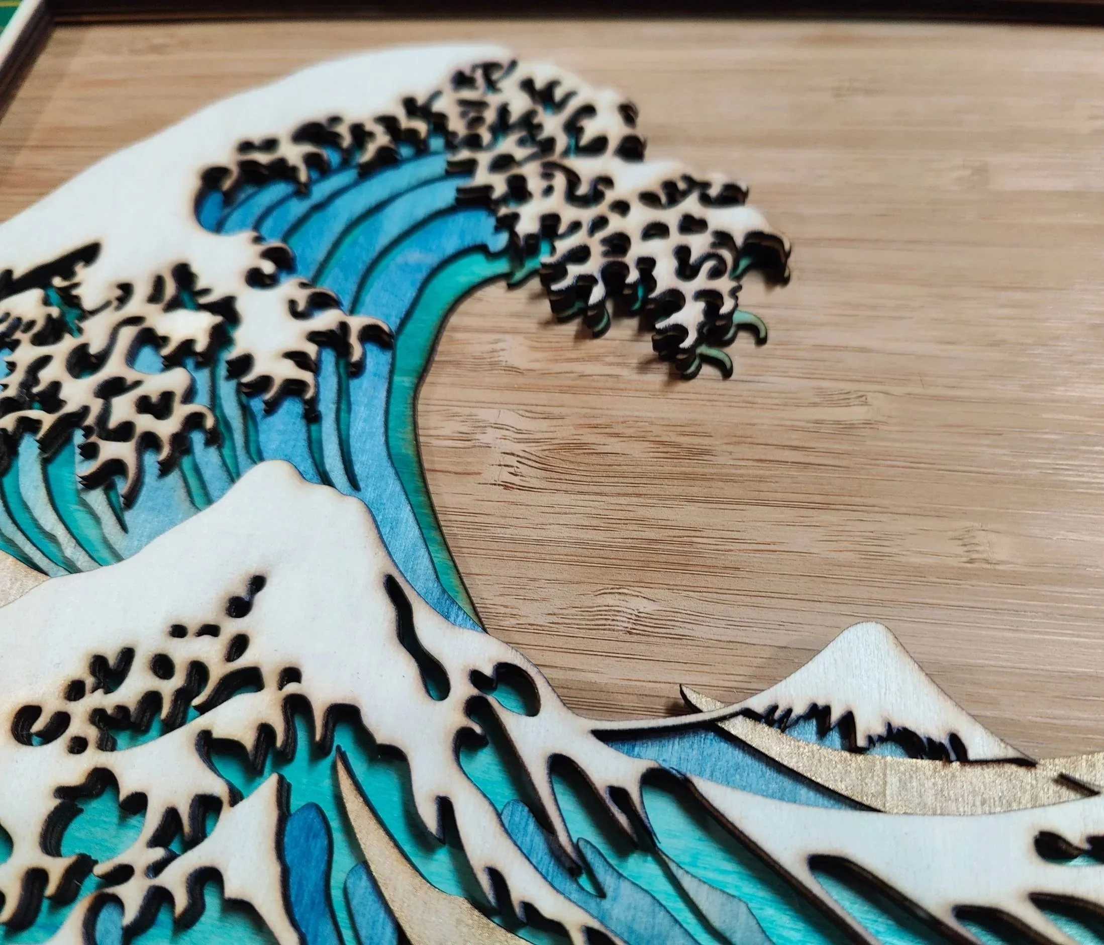 A 3d wooden surface with multiple, overlaid artistic cutout of a breaking wave design, featuring blue and white outlines and accents.  The wave is mounted on a brown bamboo veneer base
