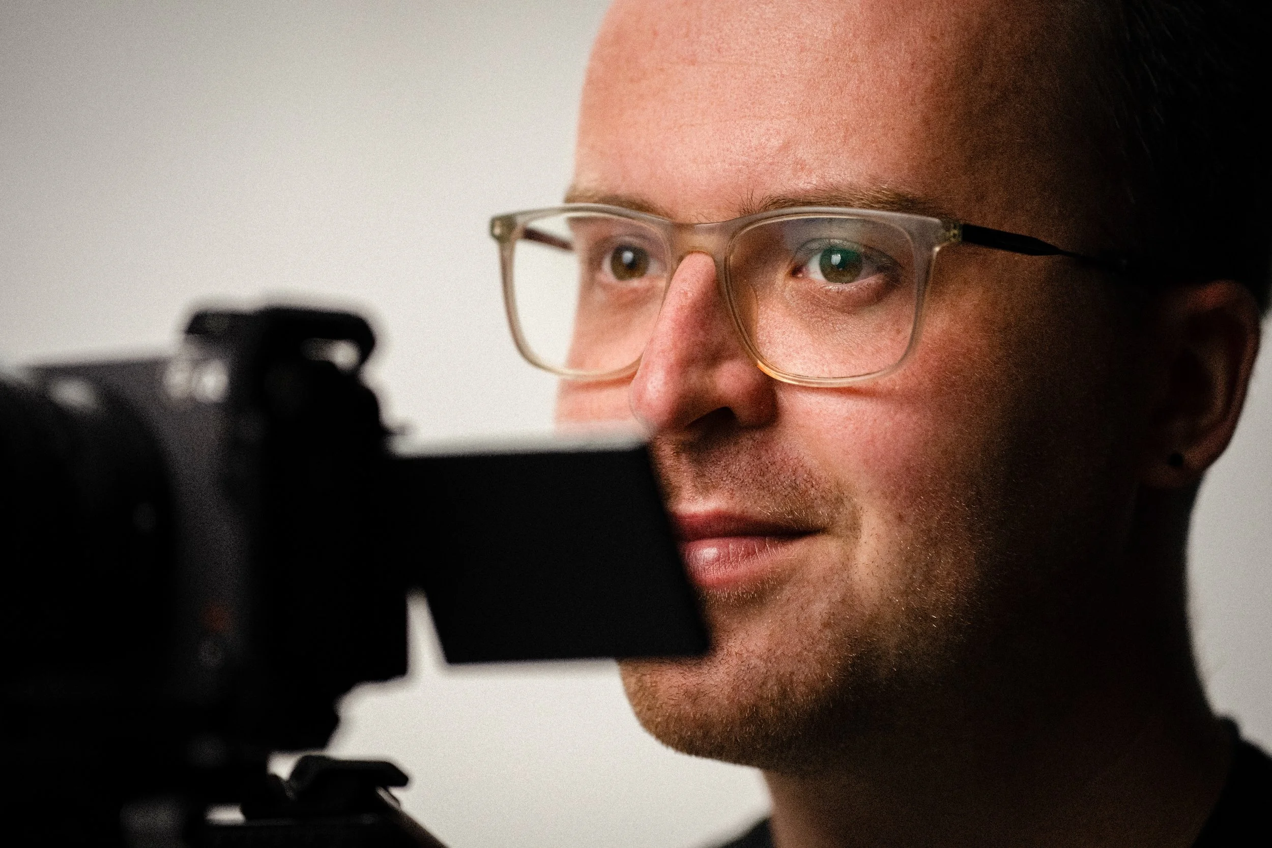 Nahaufnahme eines Mannes mit Brille, der eine Kamera betrachtet.