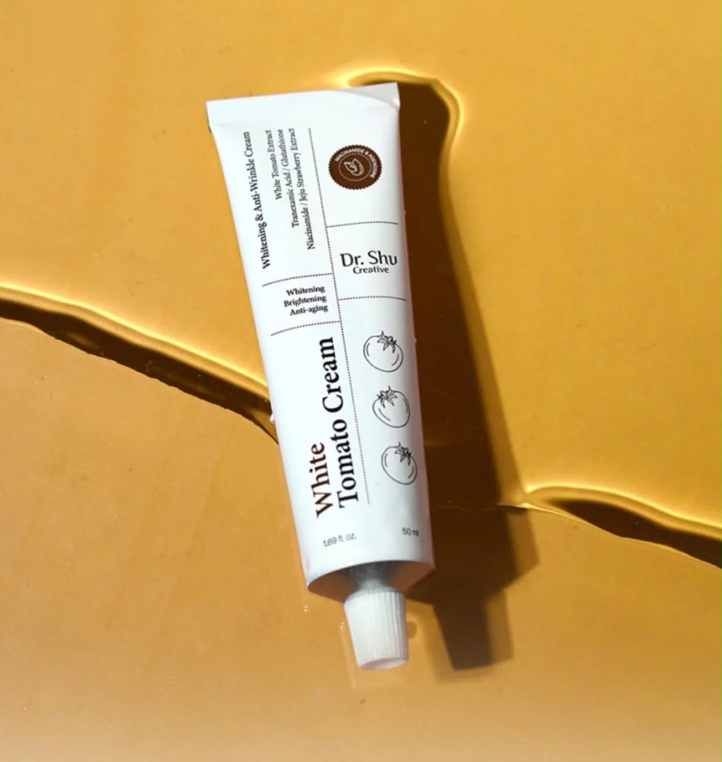 A tube of Dr. Shu White Tomato Cream, a skincare product, resting on a gold reflective surface.