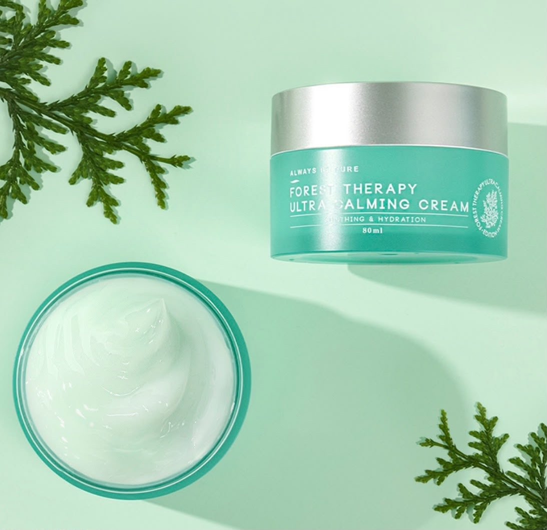Open jar of Forest Therapy Ultra Calming Cream with green leaves on light green background.