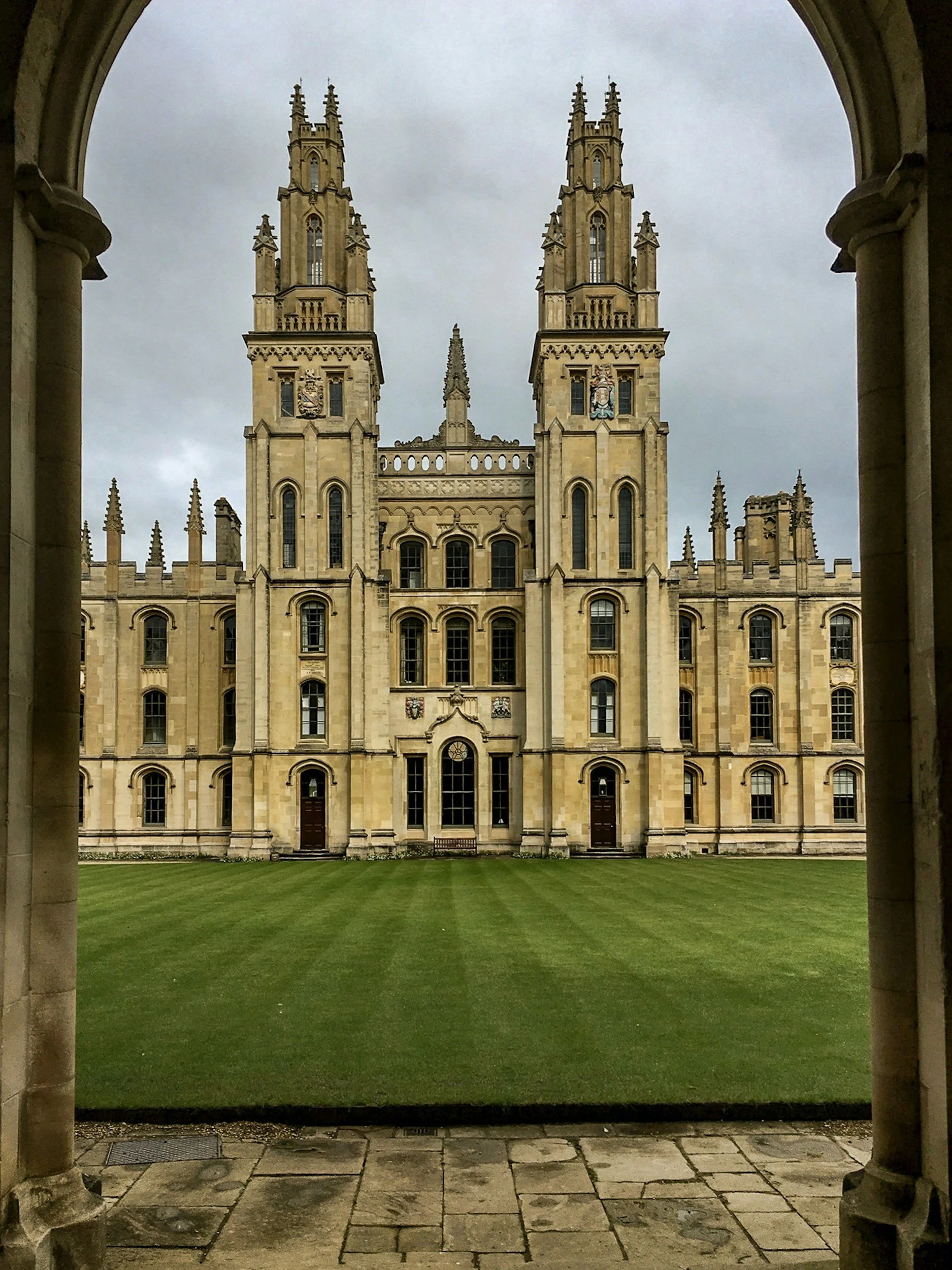 A screenshot of Oxford University's All Souls College, viewed through an stone archway looking into the Great Quadrangle towards its distinctive twin Gothic towers (known as the Hawksmoor Towers).