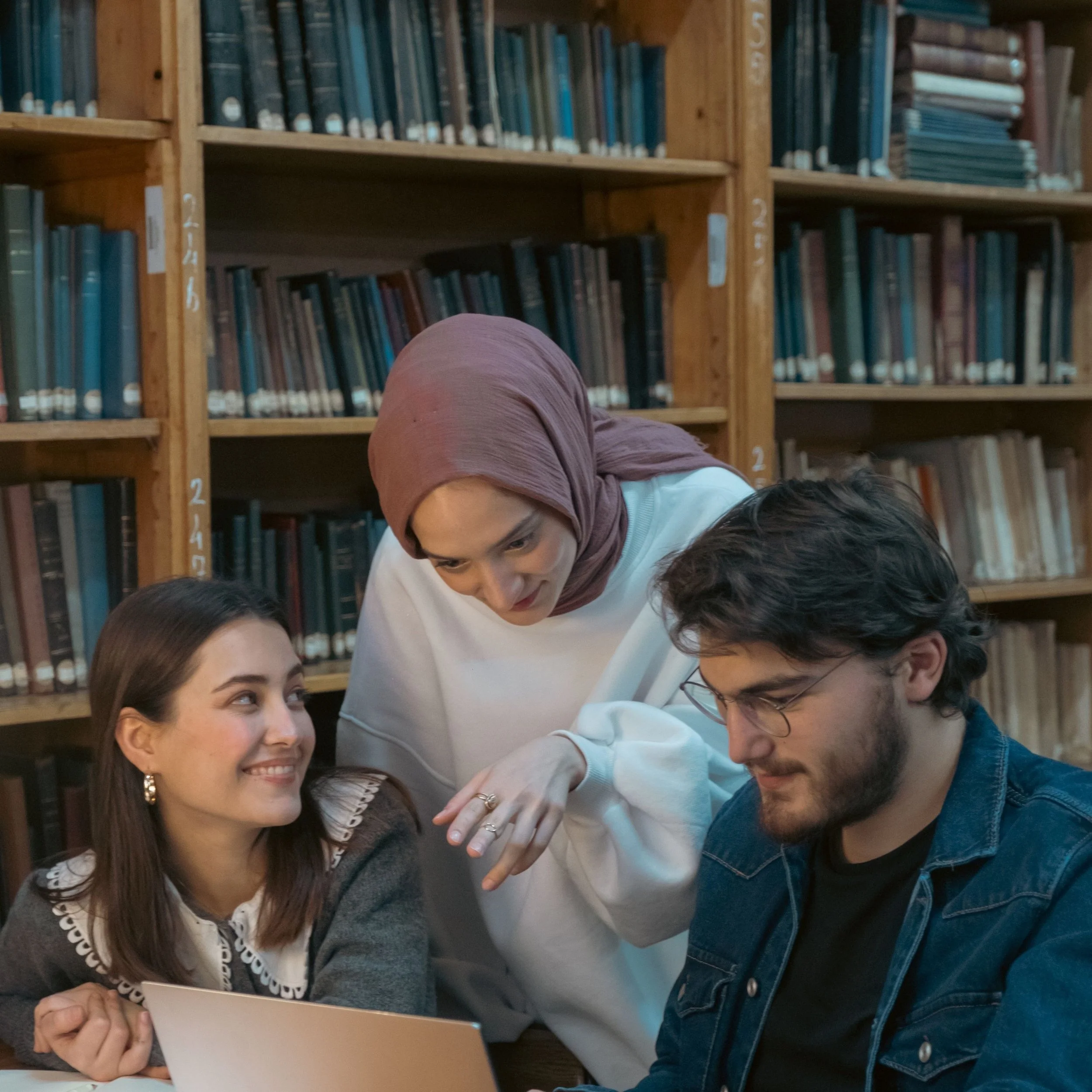 Three students working together around a laptop in a library.