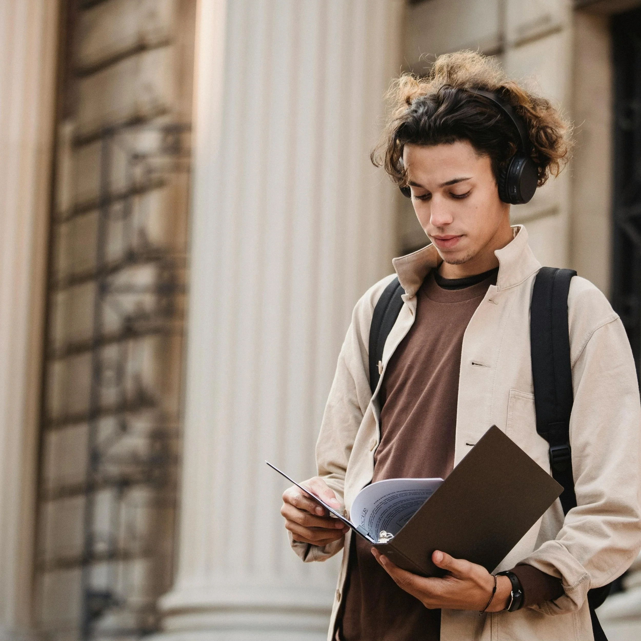 Student wearing headphones and reading from an open folder outdoors.