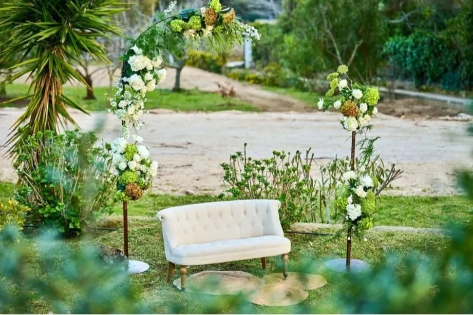 Un espacio al aire libre decorado con un armazón floral en forma de círculo, un sofá blanco y algunas plantas verdes.