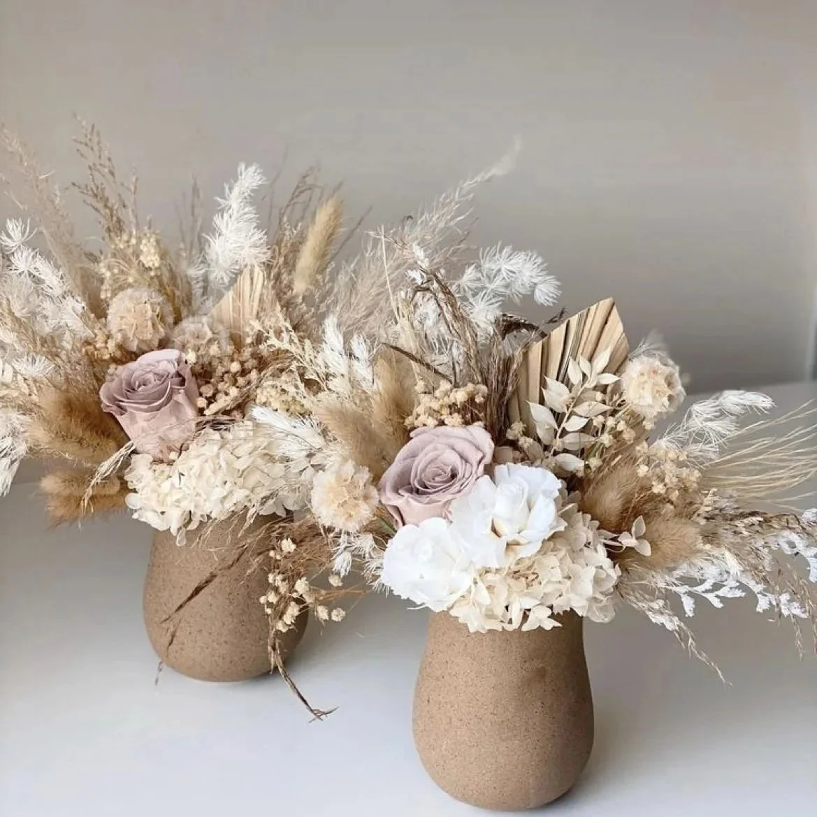 Arreglos florales en jarrones de cerámica beige con rosas, hortensias, grecas y ramas secas en tonos neutros.