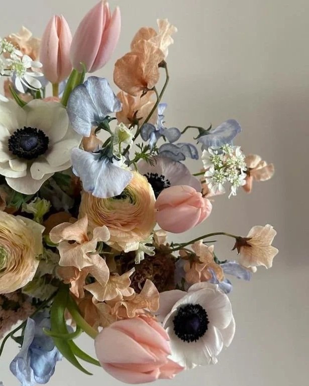 Ramo de flores con tulipanes rosados, anémonas blancas con centros negros, y flores en tonos pastel como azul, lavanda y melocotón.