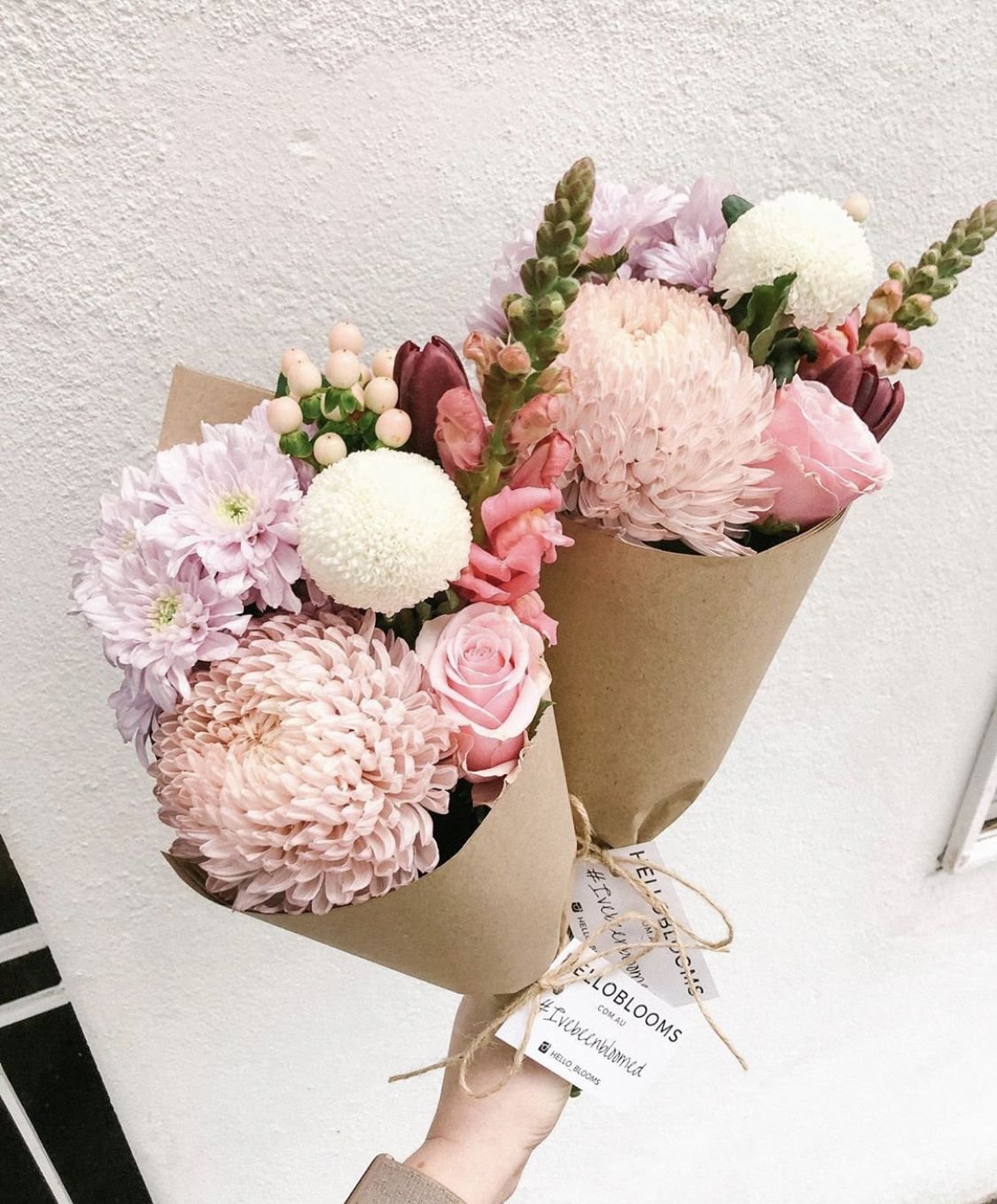 Ramo de flores con rosas, crisantemos, y otras flores en tonos rosados y blancos, envuelto en papel kraft