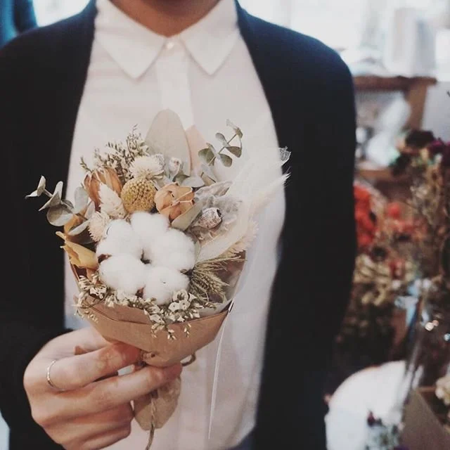 Persona sosteniendo un ramo de flores secas y algodón en una tienda de flores.