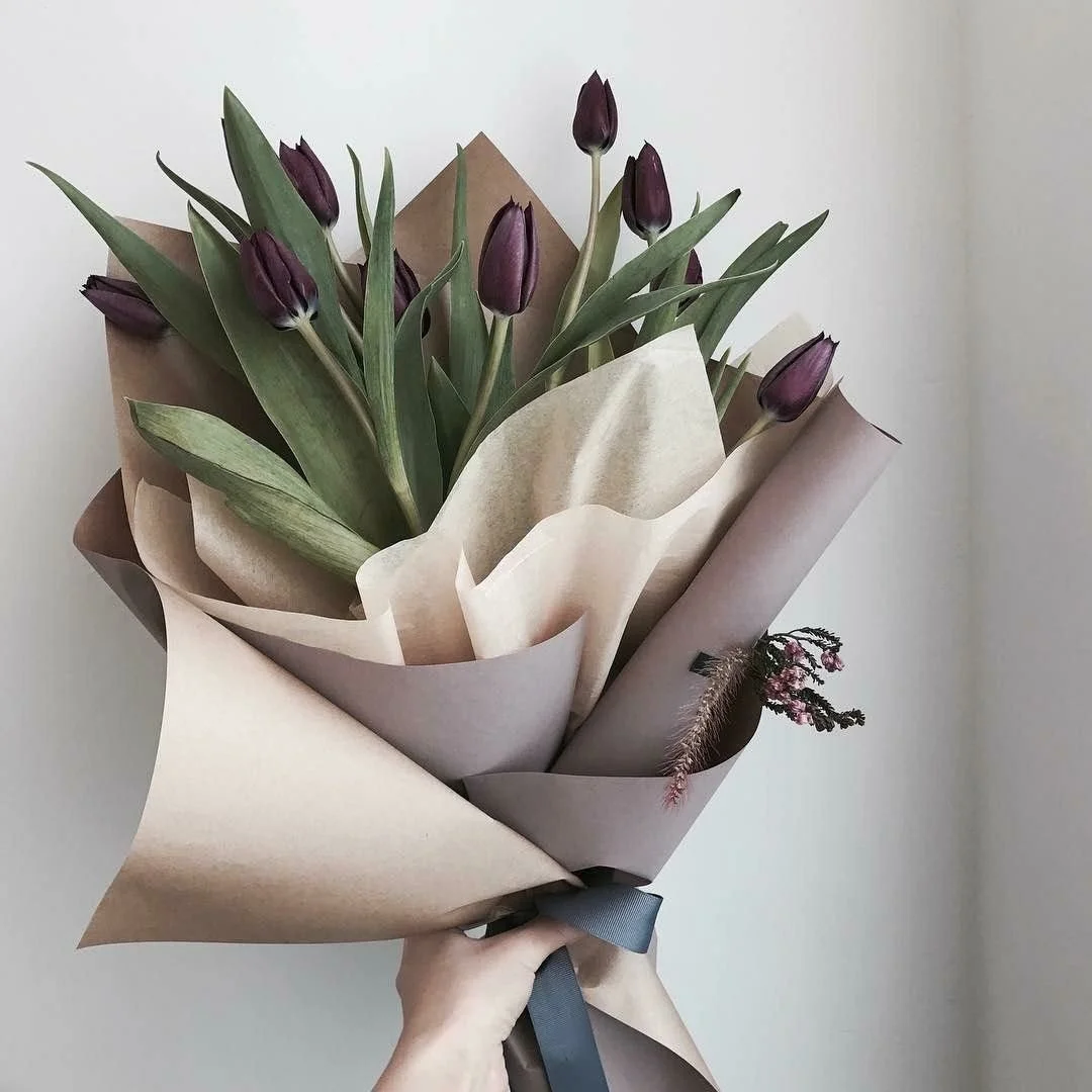 Ramo de tulipanes morados envuelto en papel marrón y cinta.
