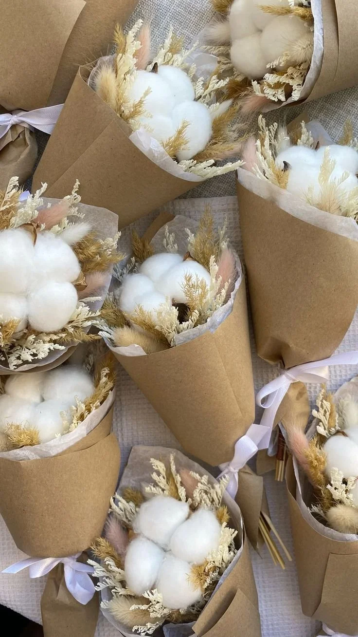 Varios arreglos florales en conos de papel marrón decorados con algodón, flores secas y orejas de conejo en tonos neutros.
