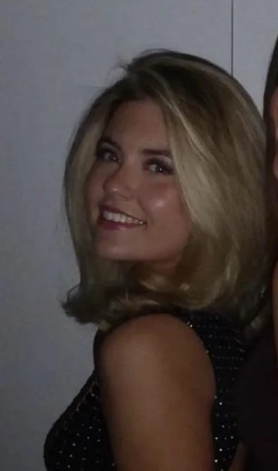 A woman with blonde hair smiling at the camera, wearing a black sleeveless top with small white polka dots.