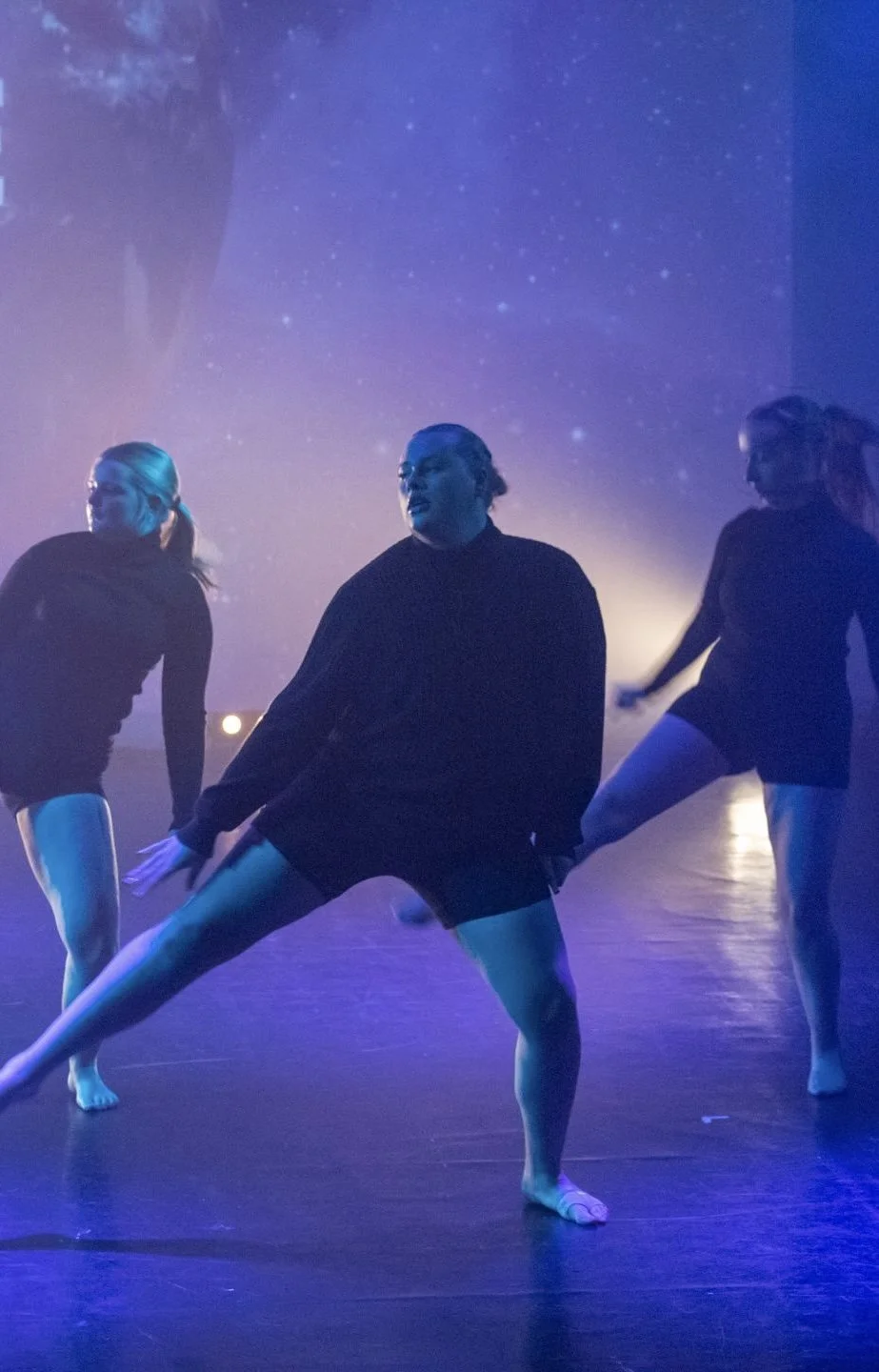 Three dancers performing on stage under purple and blue lighting with starry background.