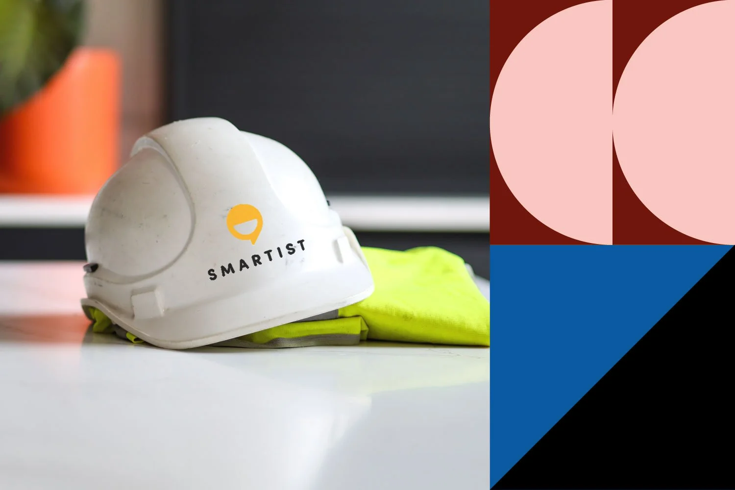Construction white hard hat with 'SMARTIST' logo, yellow safety vest, and a potted plant in the background.
