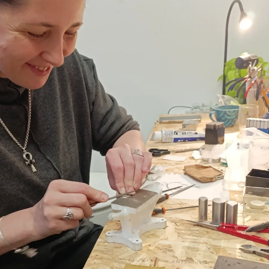 Woman working on jewelry in a jewelry workshop, using tools on a workbench with various equipment and supplies.