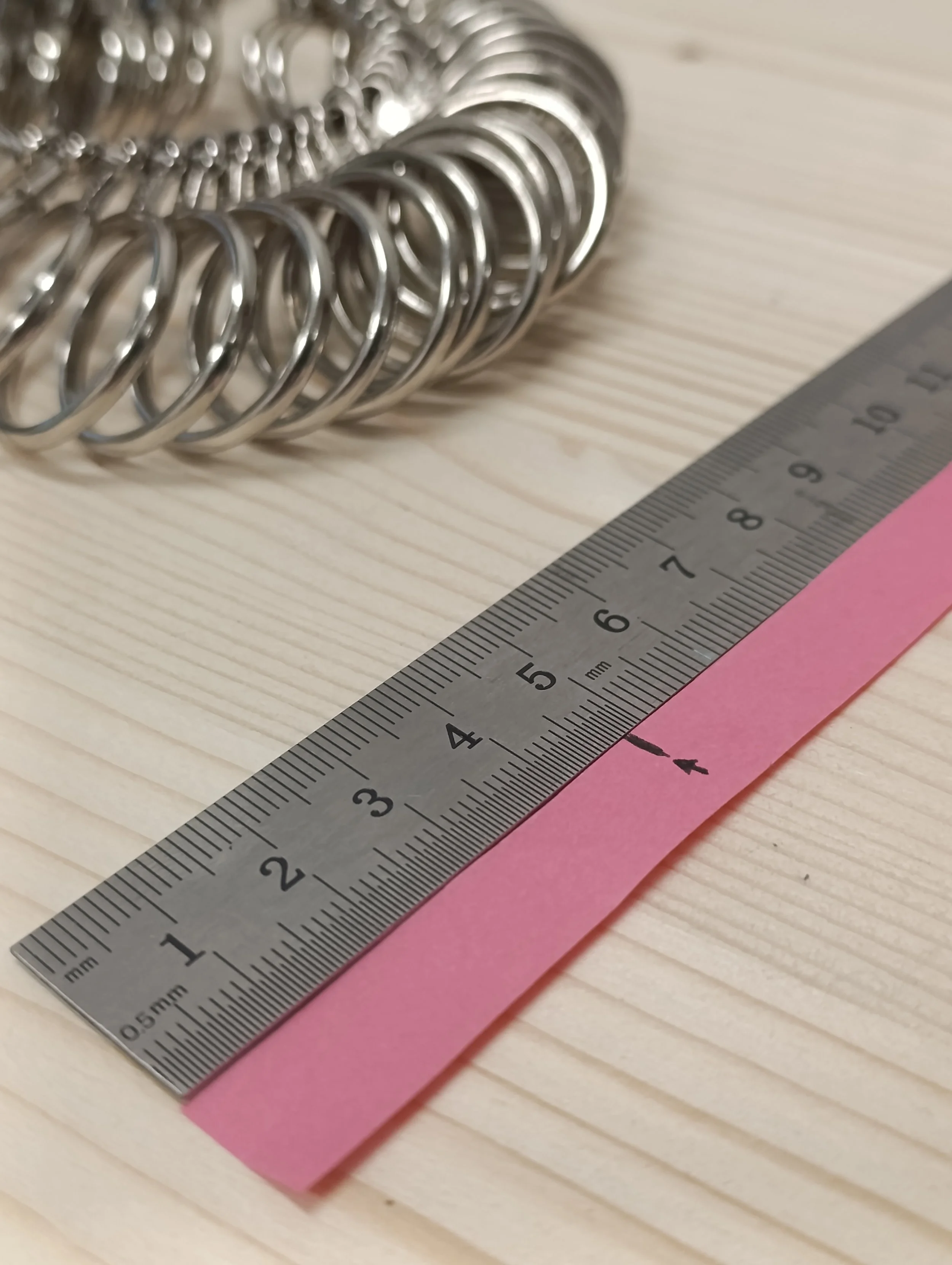 A metal ruler measuring approximately 4 inches, a pink sticky note, and a silver metal bracelet on a wooden surface.