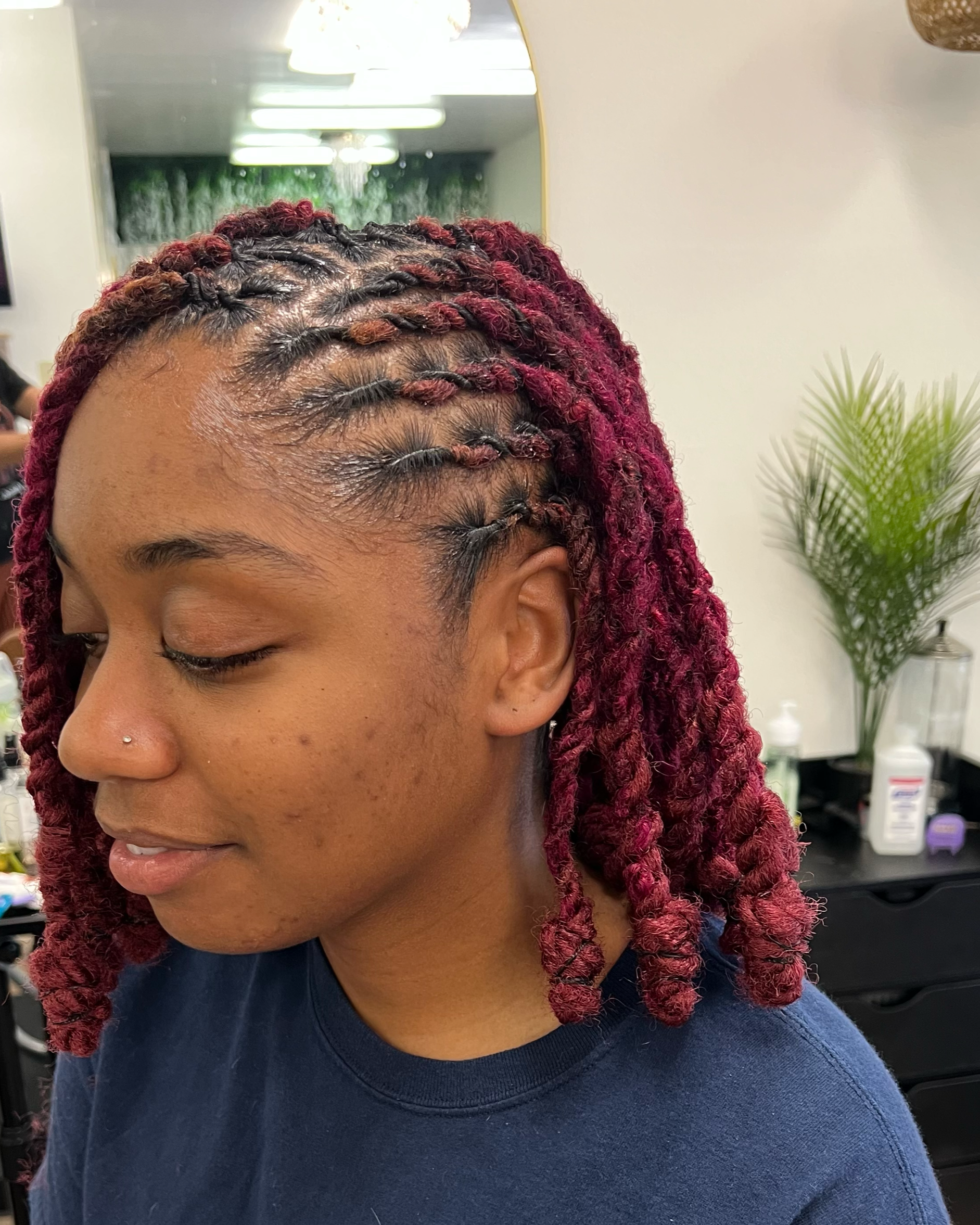 A woman with red and black yarn twists hairstyle seated in a salon.