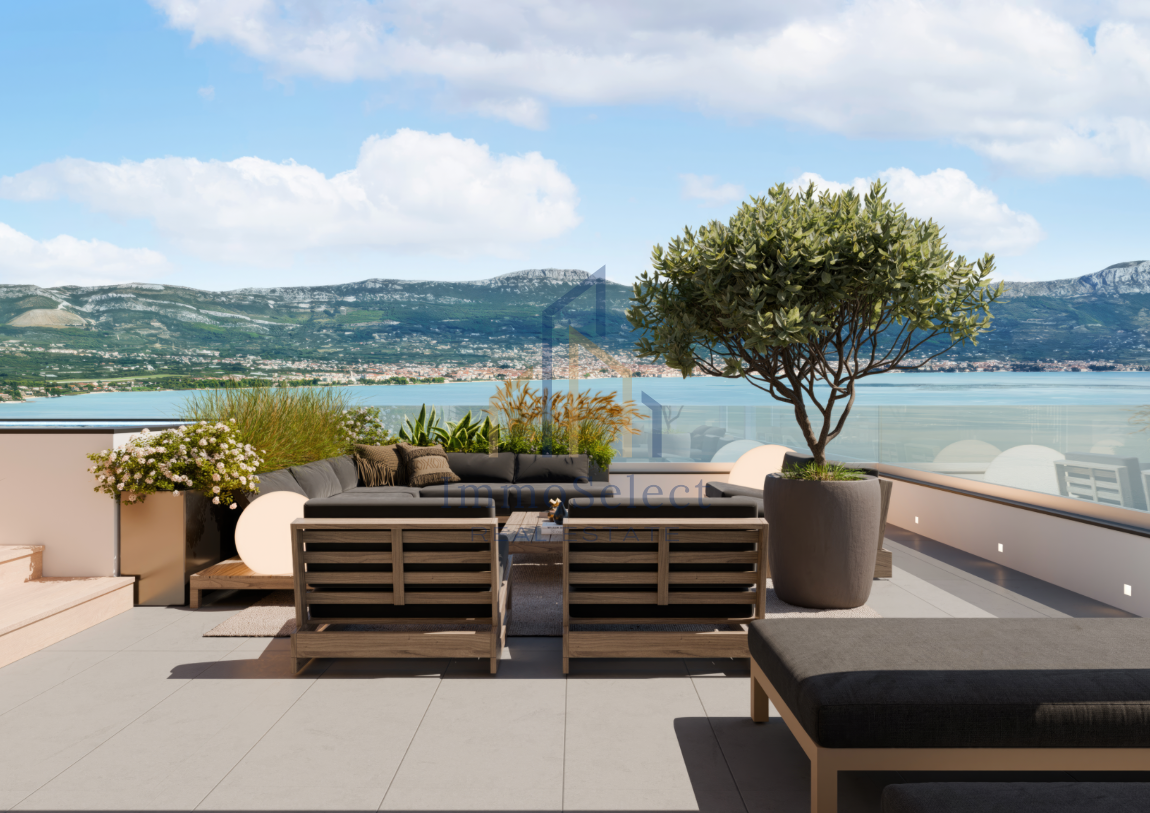 Modern rooftop terrace with outdoor seating, large potted tree, and view of a lake and mountains under a partly cloudy sky.