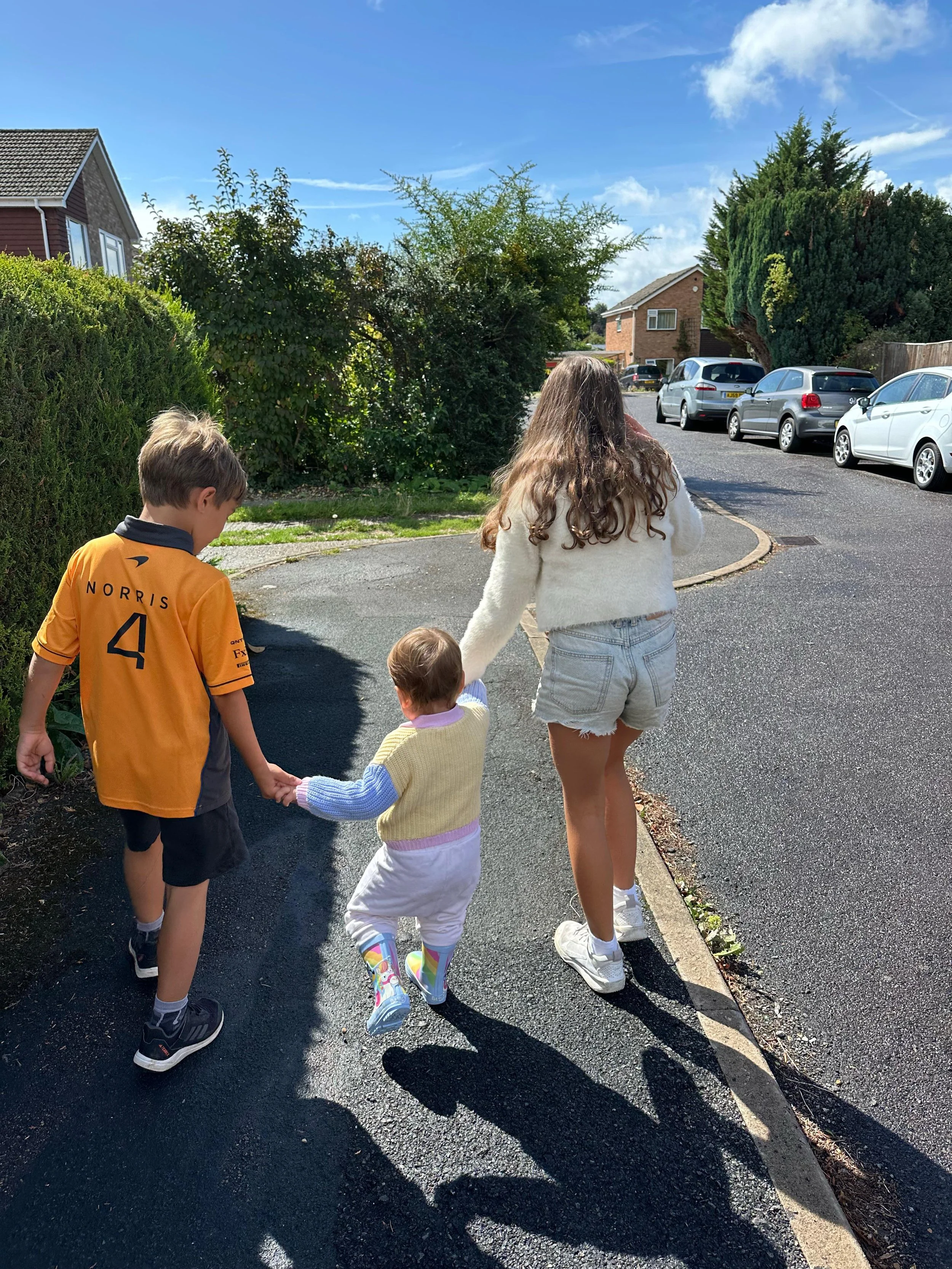 Three children walking together on a sunny day, holding hands
