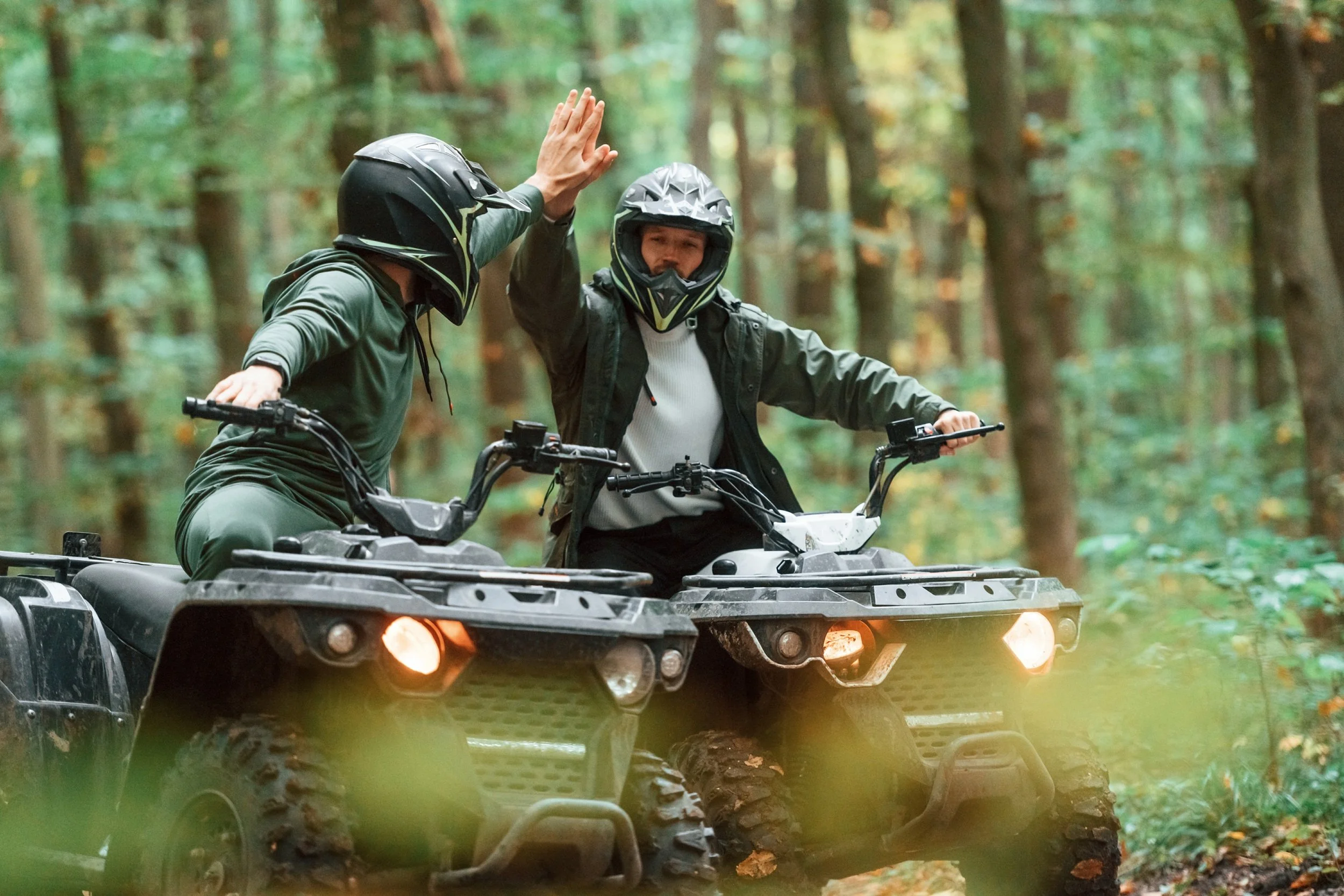 two people in the woods high fiving while each driving an ATV