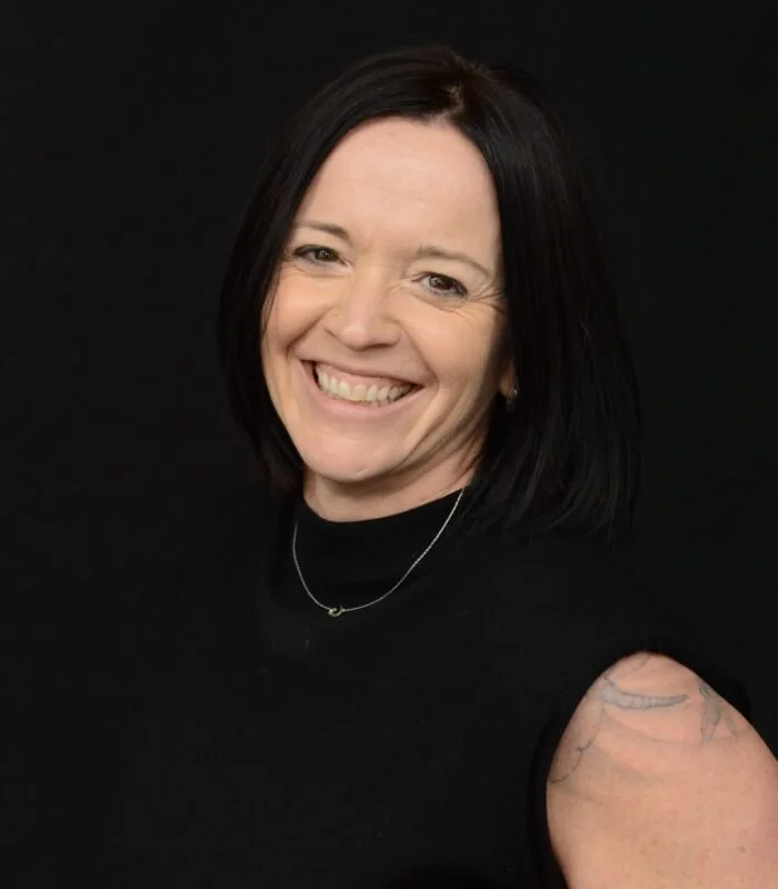 Carrie Charette headshot shoulder-length black hair smiling against a black background.
