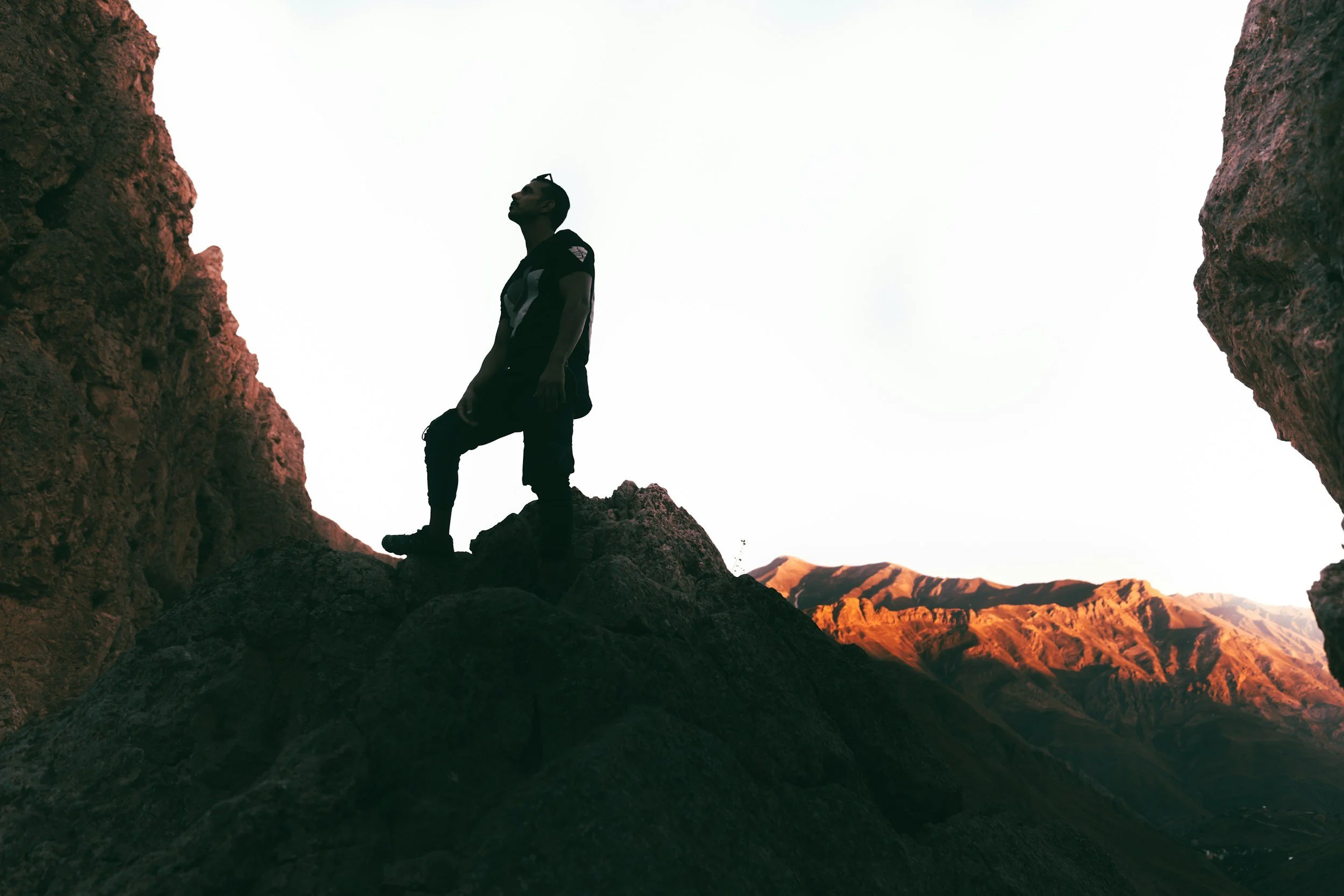 a person hiking looking up at a rock cliff with the sun just starting to rise on the mountains behind them