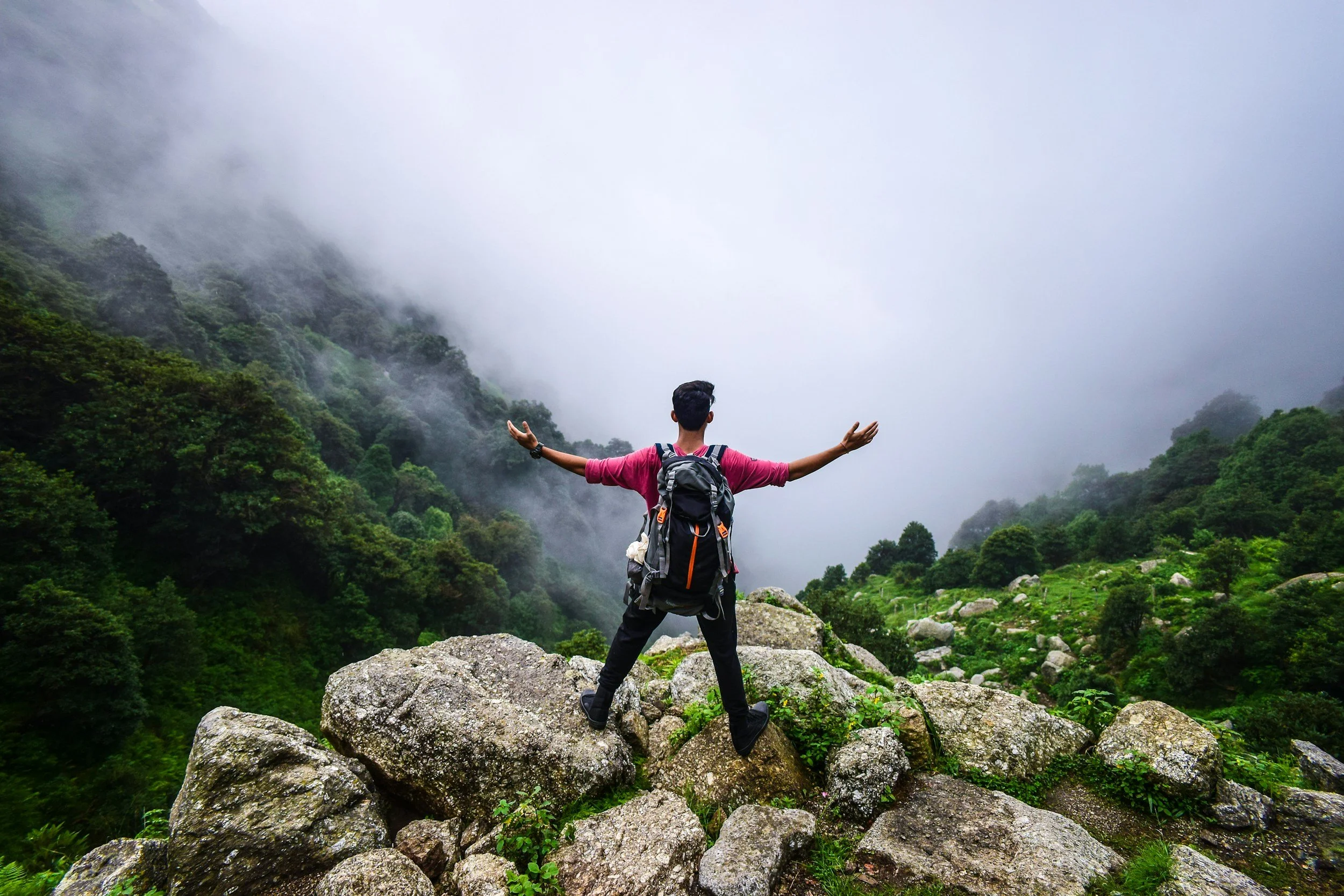 man with a backpack on top of a mountain looking out to a foggy abyss with his arms spread out