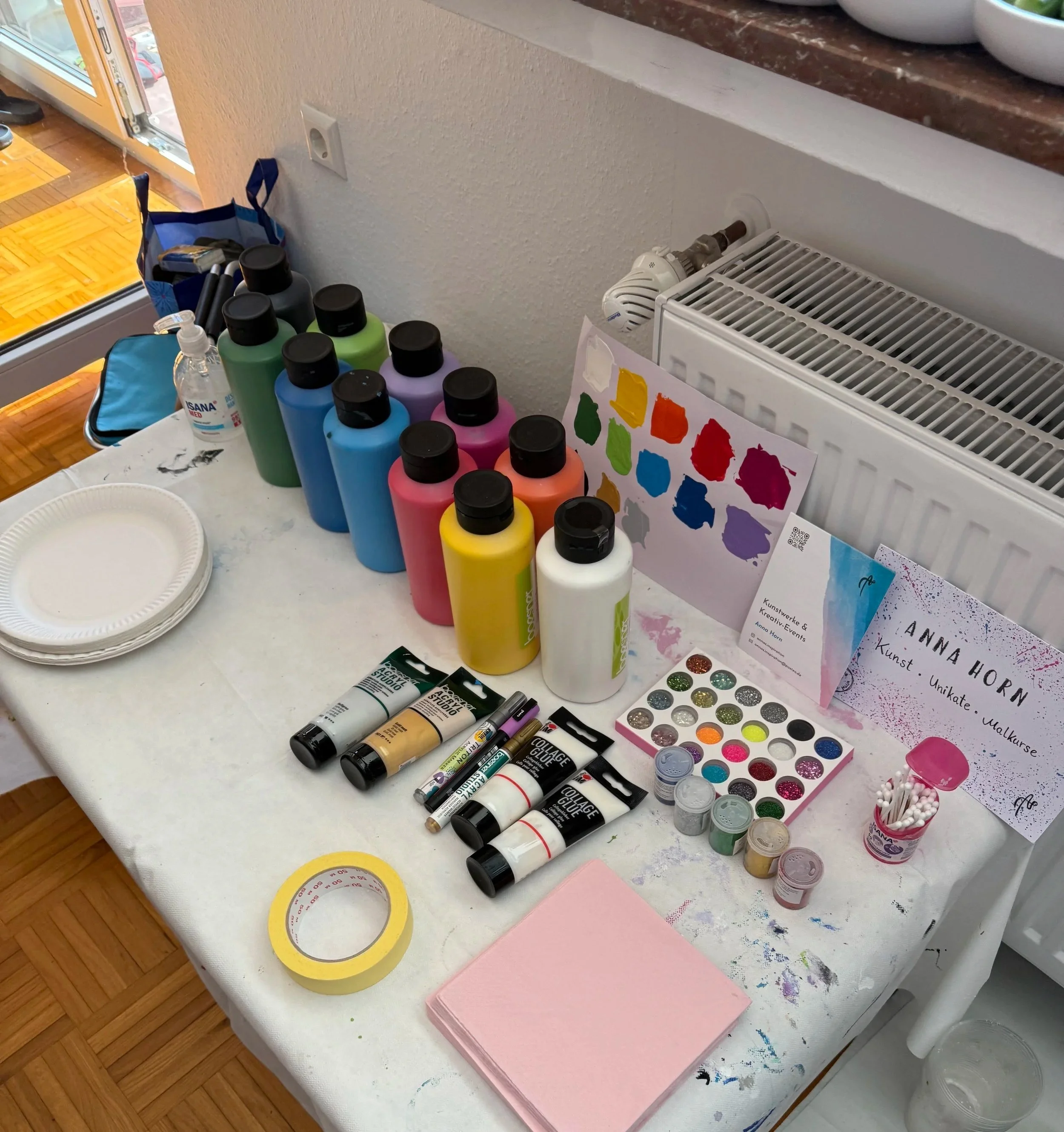 Tisch mit bunten Malfarben, Malwerkzeugen, Papiertüchern und Kunstmaterialien, wahrscheinlich für einen kreativen Malkurs, Kunst-Workshop vorbereitet.