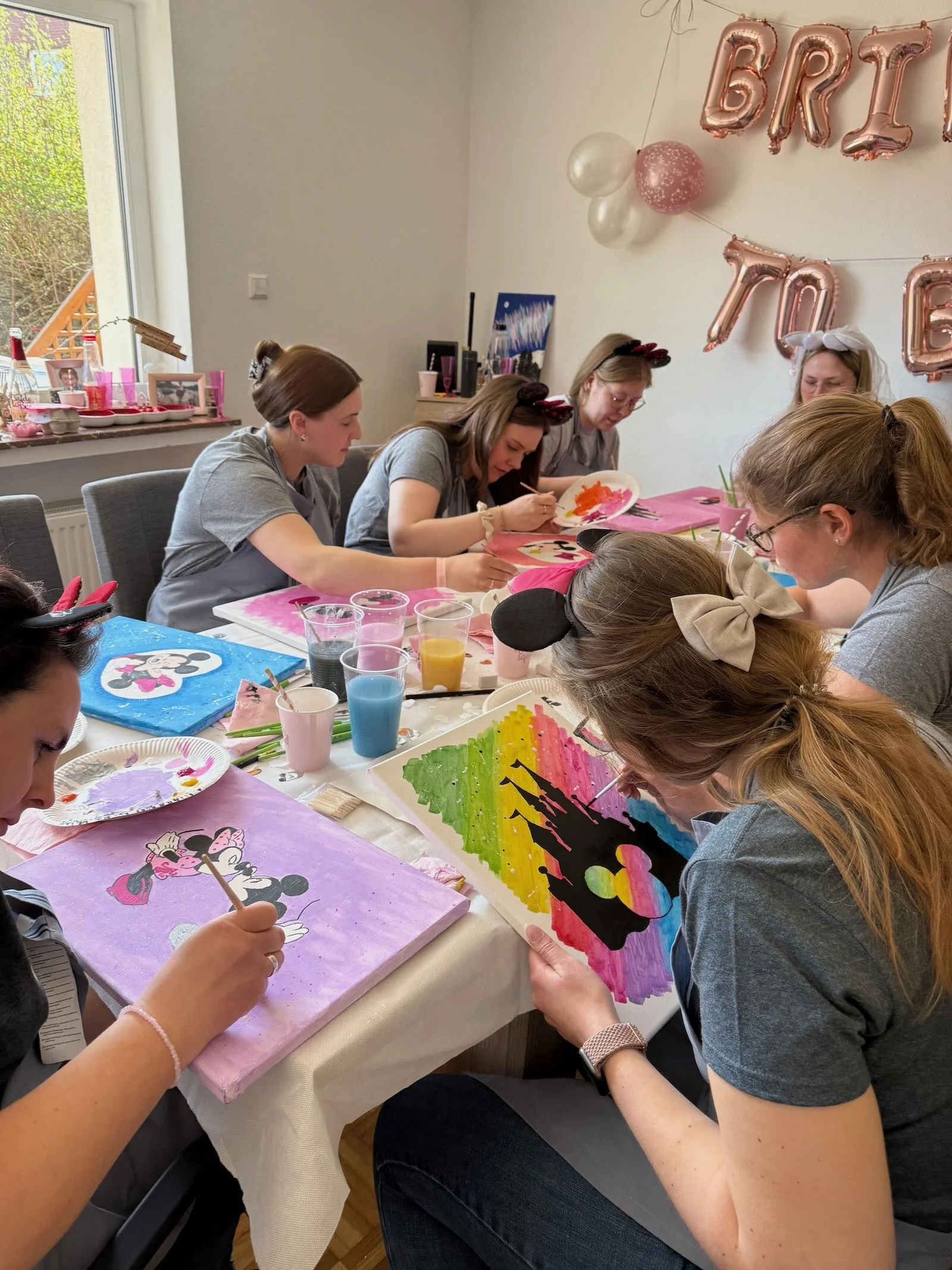 Eine Gruppe von Frauen bemalt auf Leinwänden mit Disney-Motiv, vermutlich Minnie Mouse, bei einer kreativen Malkurst, Kunst-Workshop in einem hellen freundlichen Raum.