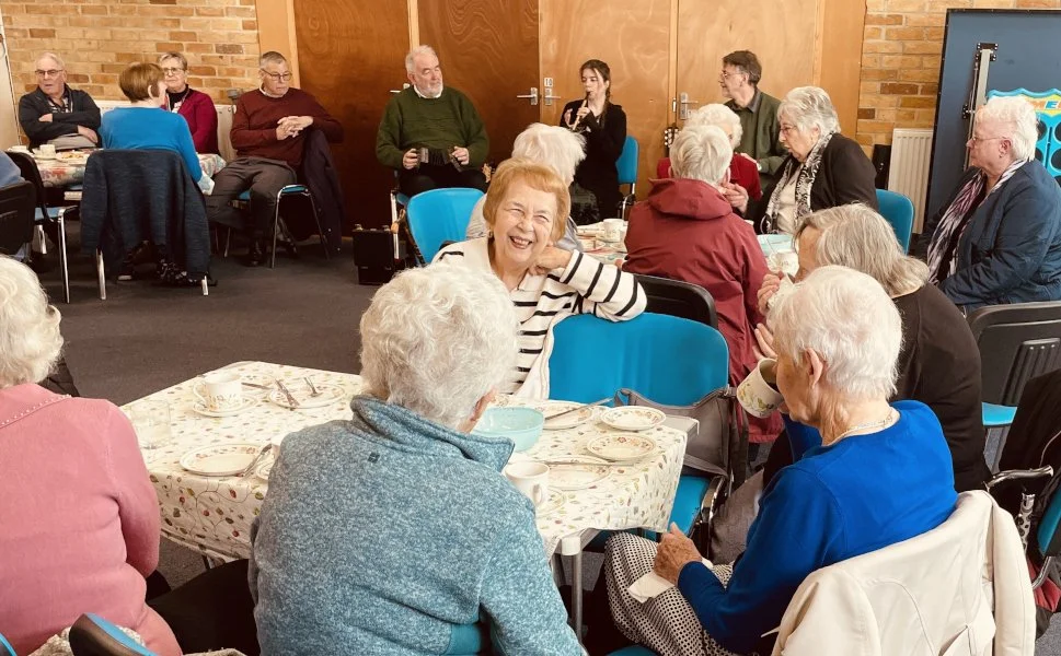 Local senior citizens enjoying a cream tea with musical entertainment after their country drive